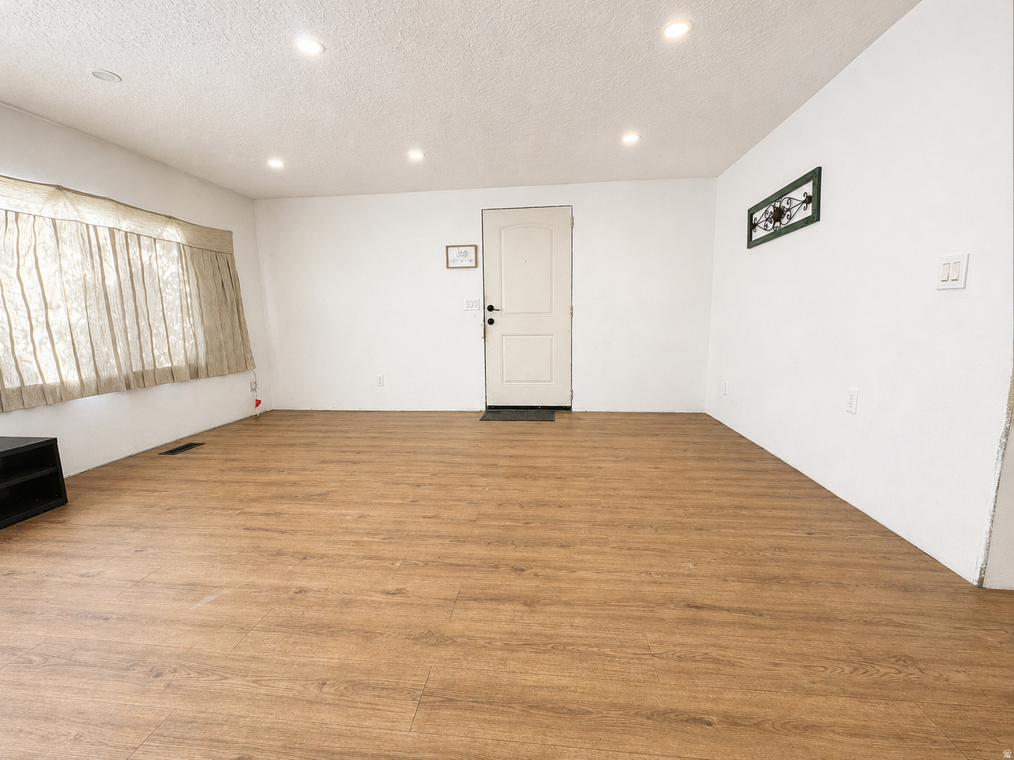 Spacious room featuring wood-finish flooring and recessed ceiling lighting