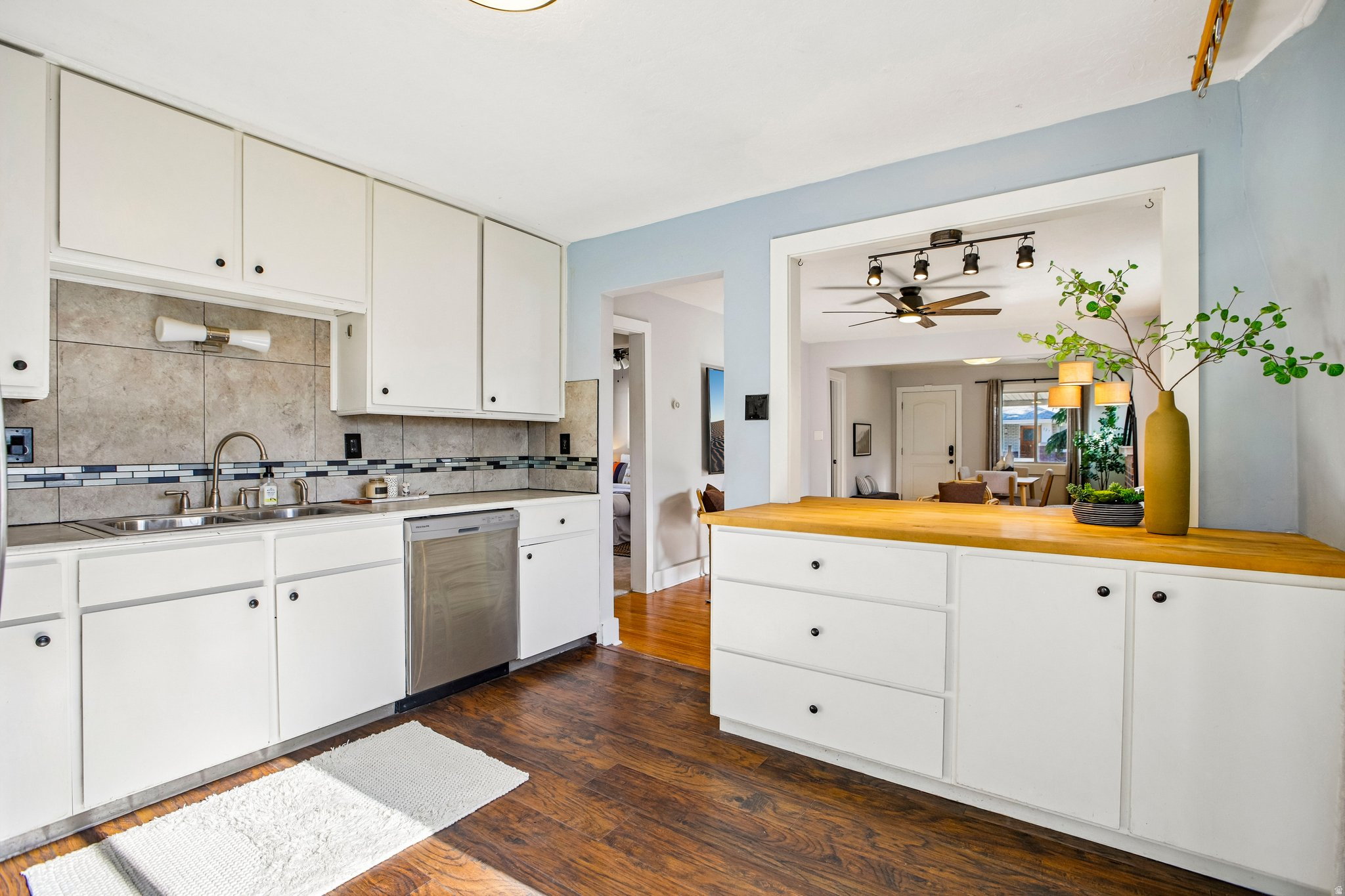 Kitchen featuring white cabinetry, stainless steel dishwasher, tile backsplash, and wood-finish flooring