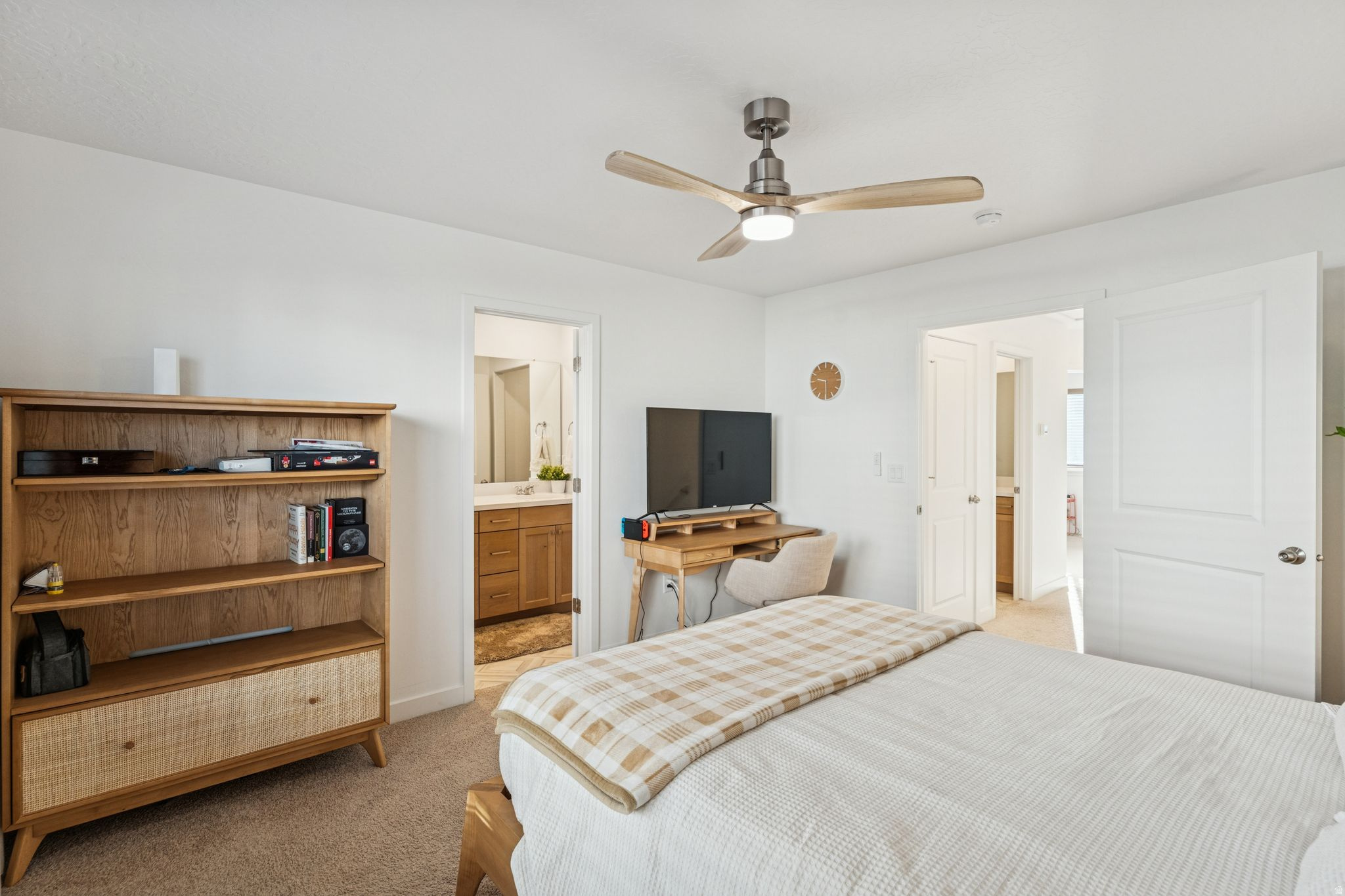 Bedroom featuring light-colored carpeting, a ceiling fan with integrated lighting, and a doorway leading to a bathroom with a vanity and mirror