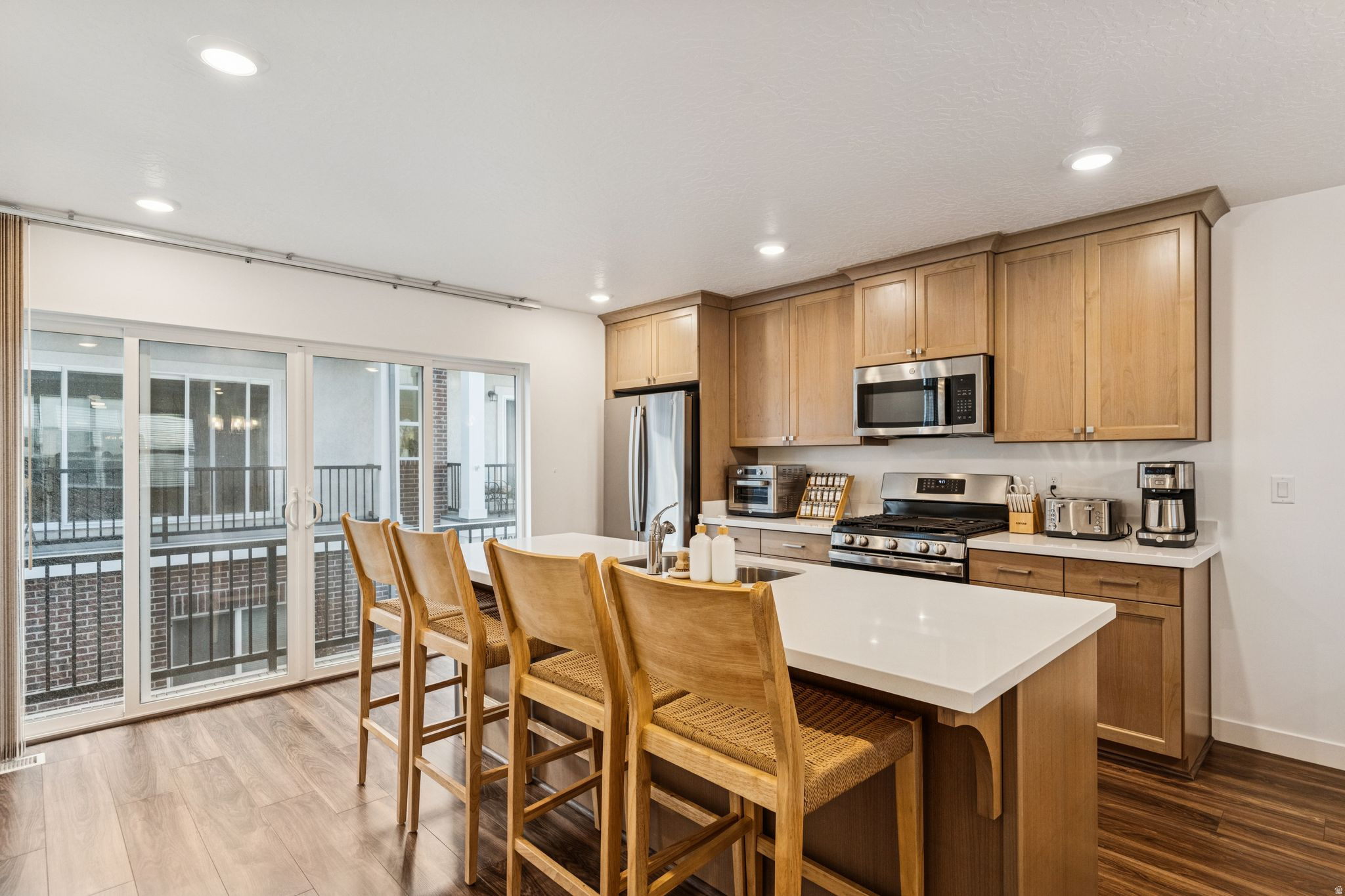 Modern kitchen featuring light wood cabinetry, stainless steel appliances, and a central island with white countertops