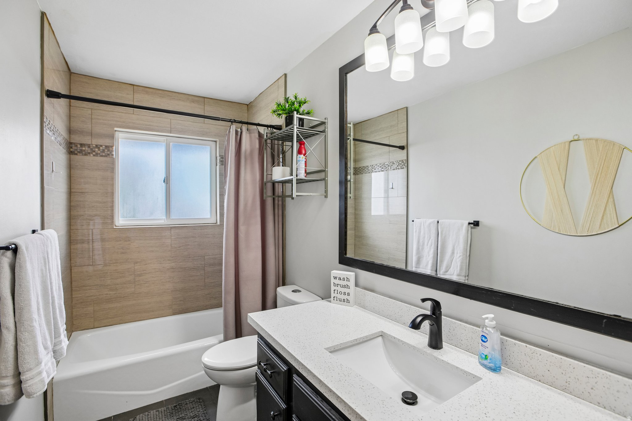 Bathroom featuring a tub/shower combination with subway tile surround and decorative accent band, a single window, and a dark-finish vanity with a light-tone countertop and integrated sink