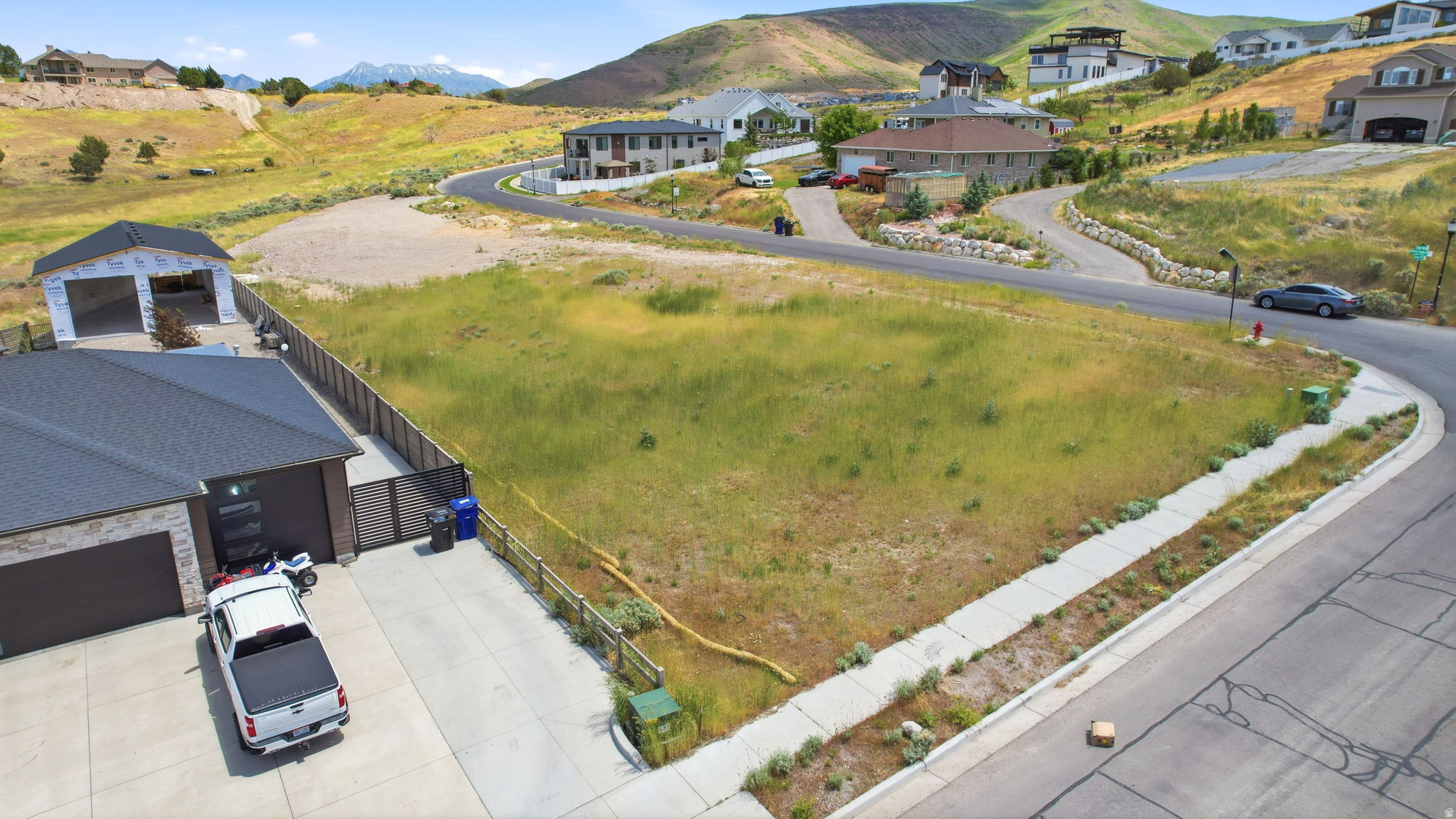 Expansive buildable lot featuring a natural grass landscape, concrete sidewalk, and mountain backdrop