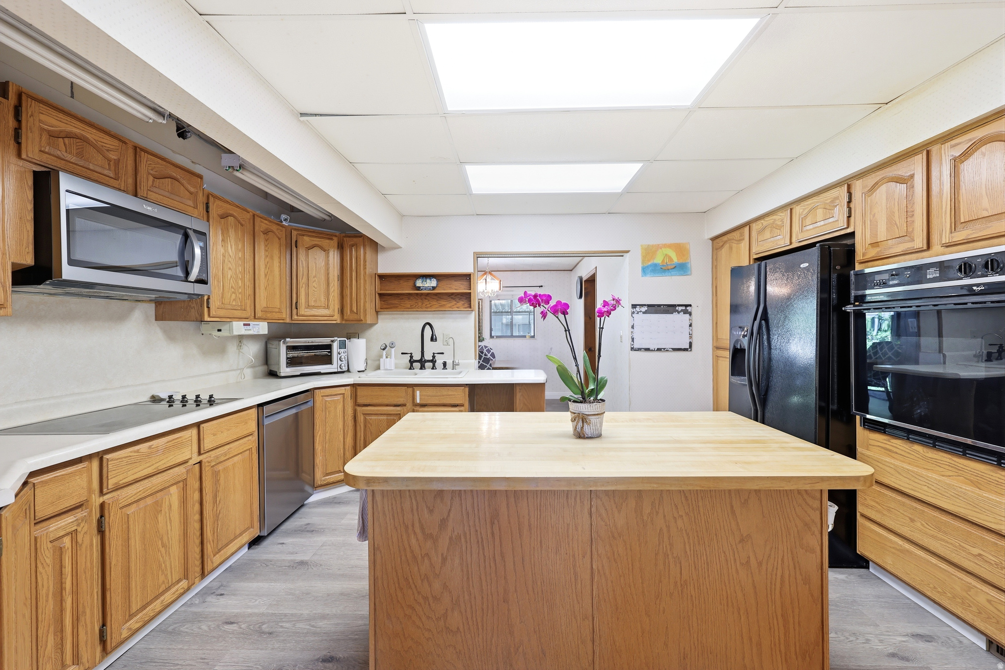 Kitchen featuring a central island with a butcher block countertop, wood-finish cabinetry, built-in wall oven, and stainless steel dishwasher