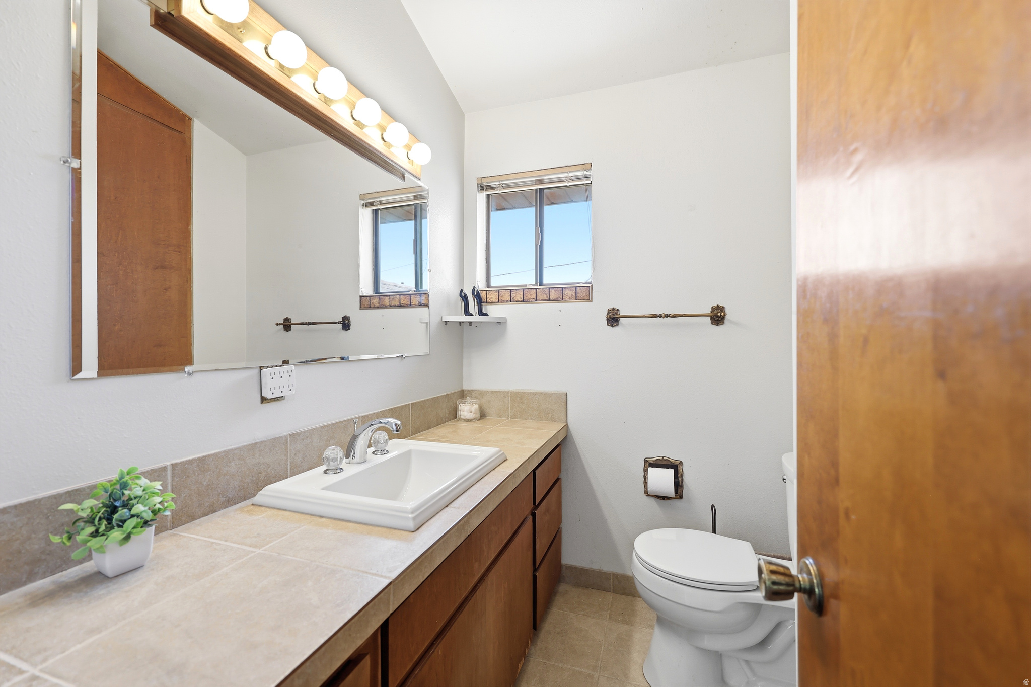 Bathroom featuring a rectangular drop-in sink, wood-finish cabinetry, neutral countertop, and a vanity mirror with overhead lighting