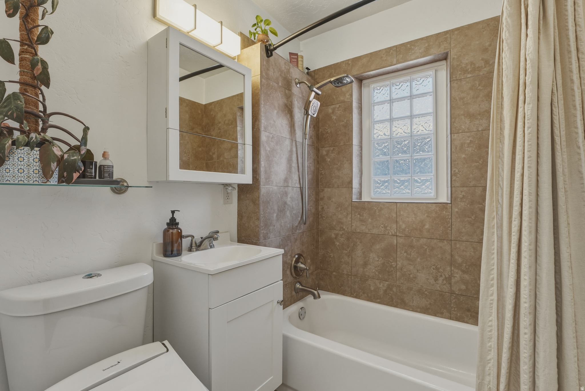 Bathroom featuring a white vanity with integrated sink, coordinating medicine cabinet, and a glass block window in the shower area