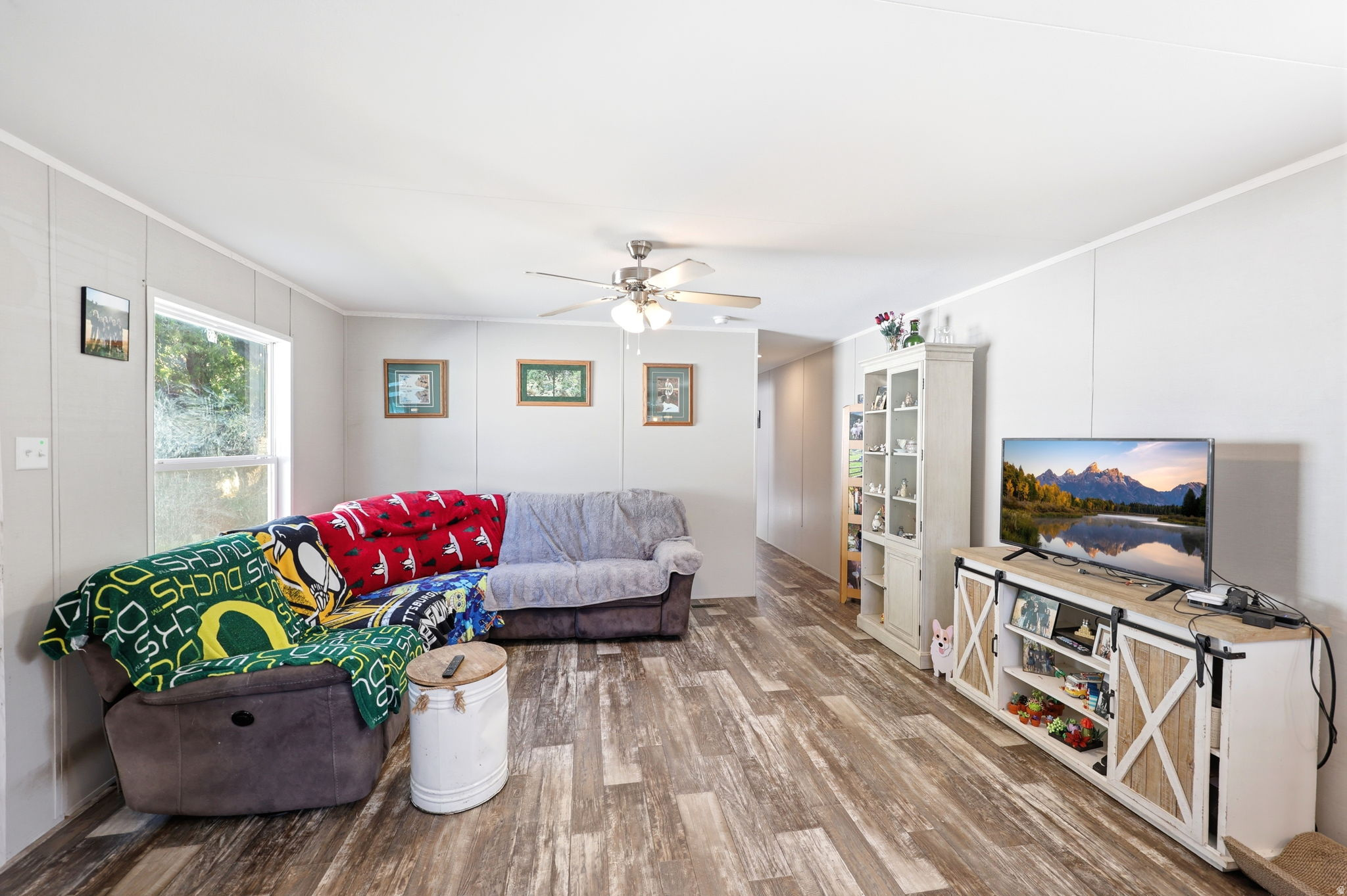 Spacious living area featuring wood-finish flooring, light-toned wall paneling, and a ceiling fan with integrated lighting