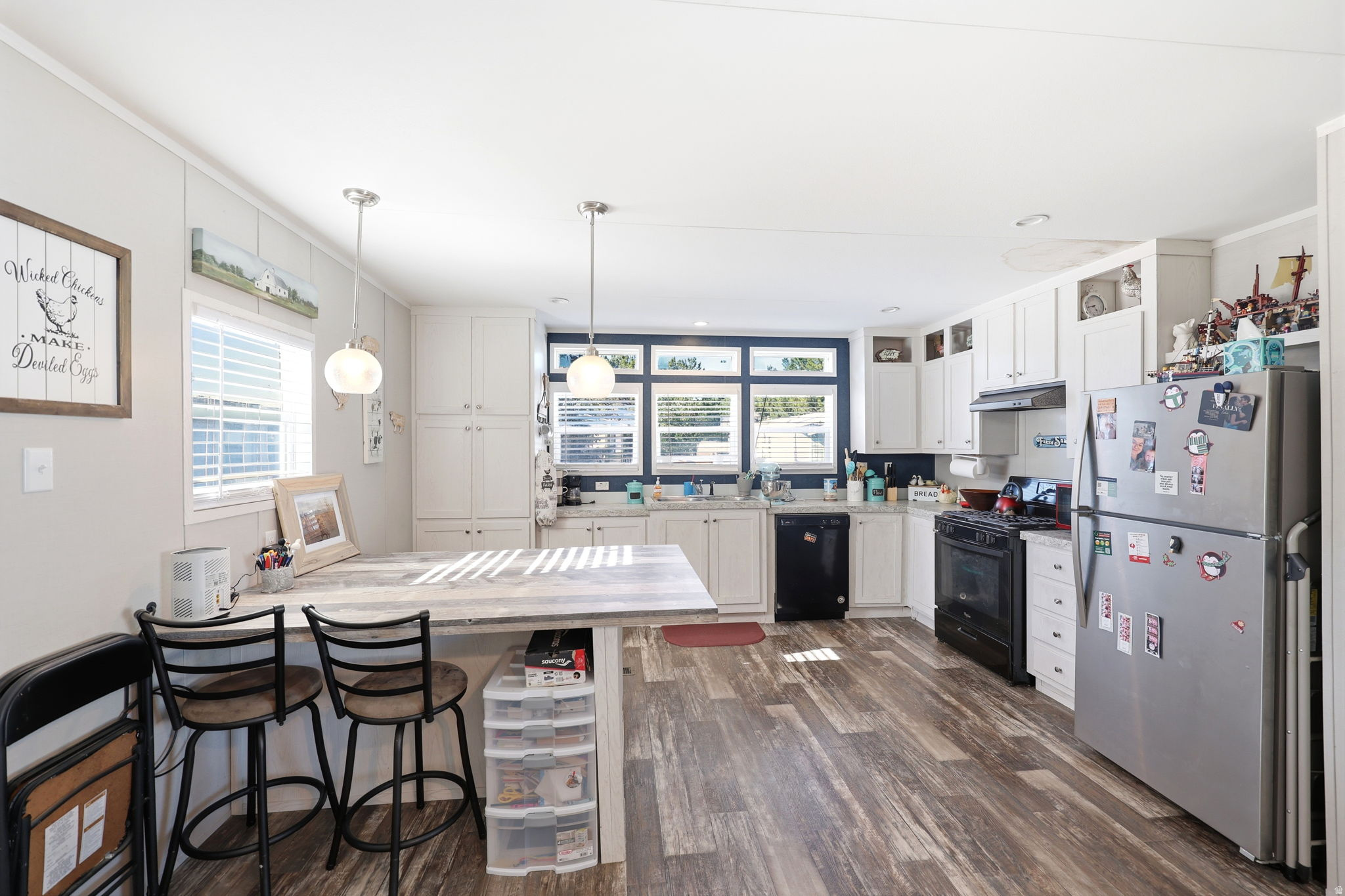Expansive kitchen featuring wood-finish flooring, white cabinetry, light-colored countertops, and a full suite of black and stainless steel appliances