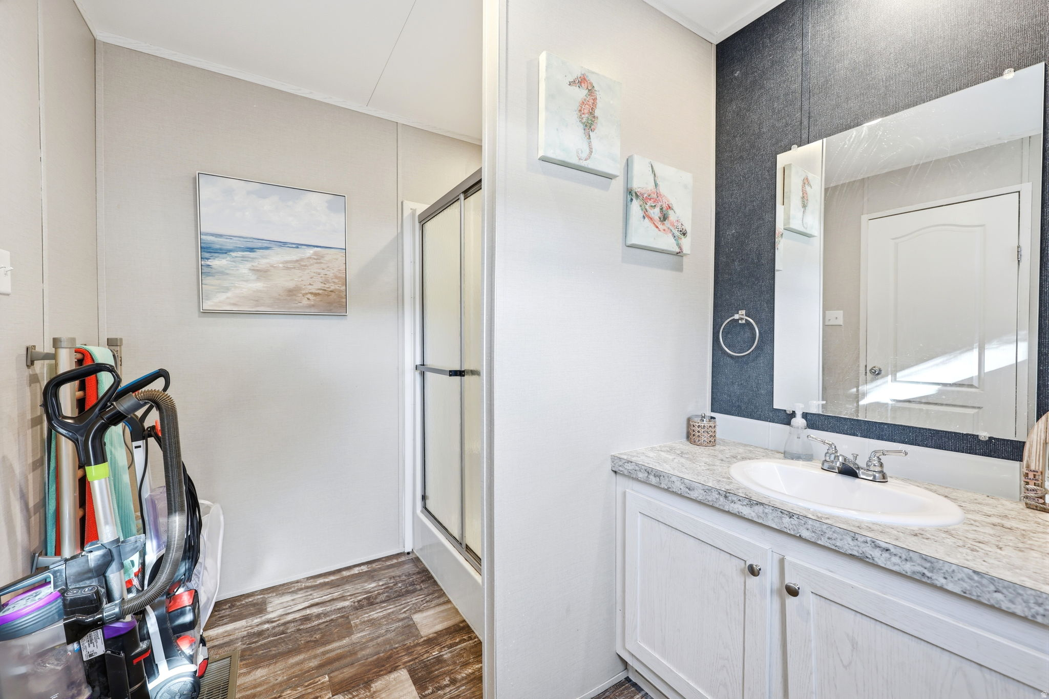Bathroom featuring a single vanity with a white countertop and oval sink, a wall-mounted mirror, and wood-finish flooring