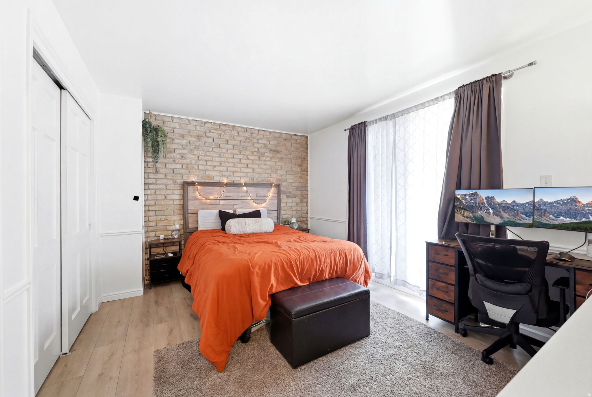 Bedroom featuring an exposed brick accent wall, wood-finish flooring, and white bifold closet doors