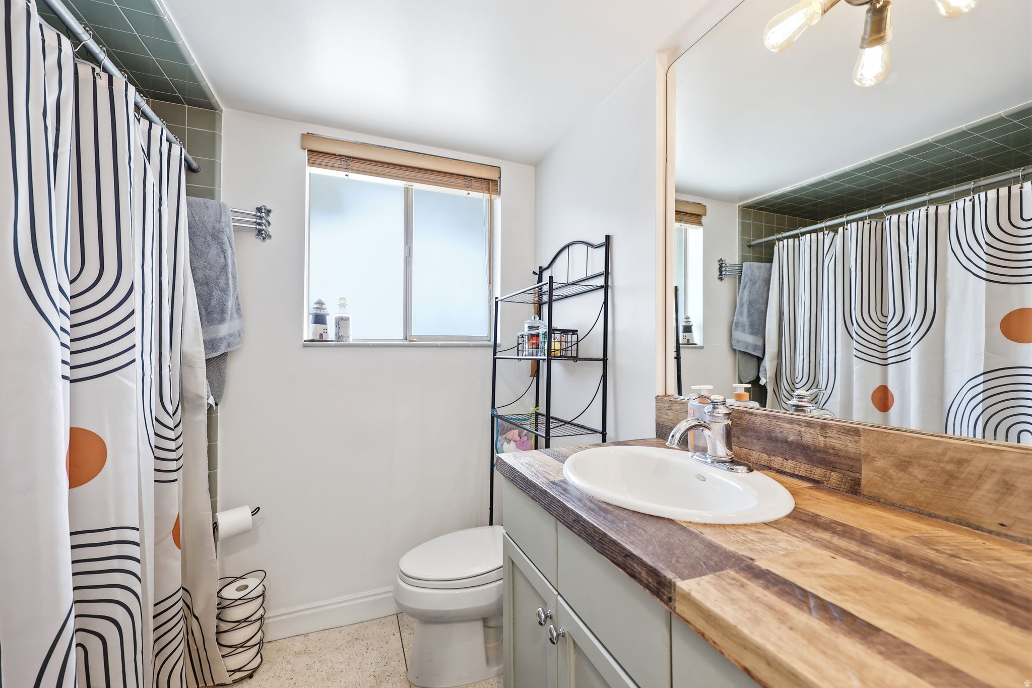 Bathroom featuring a wood-finish countertop vanity with an undermount sink, a large wall-mounted mirror, and a window with a wood-finish blind