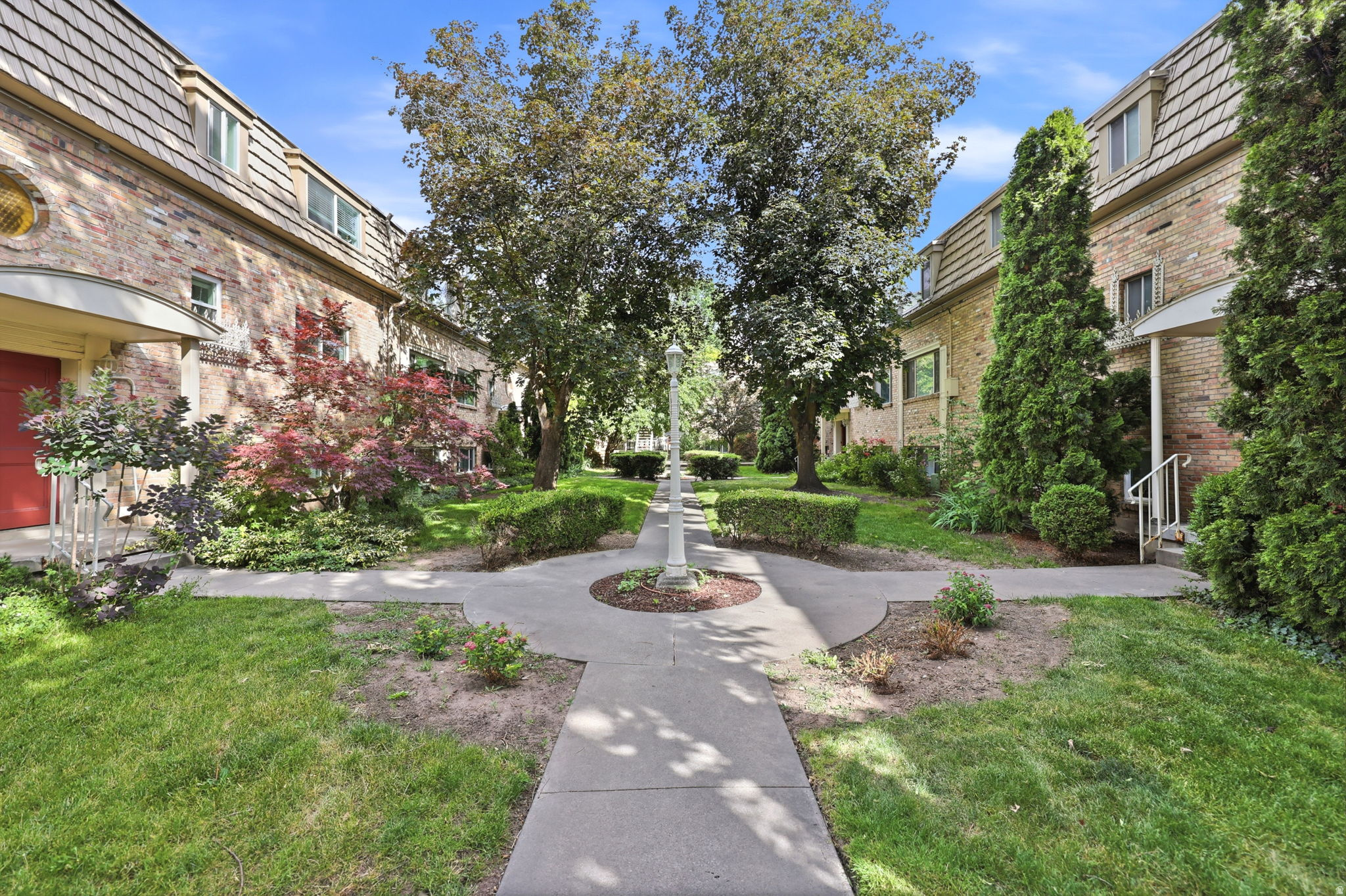 Lush courtyard featuring mature trees, manicured hedges, and paved walkways