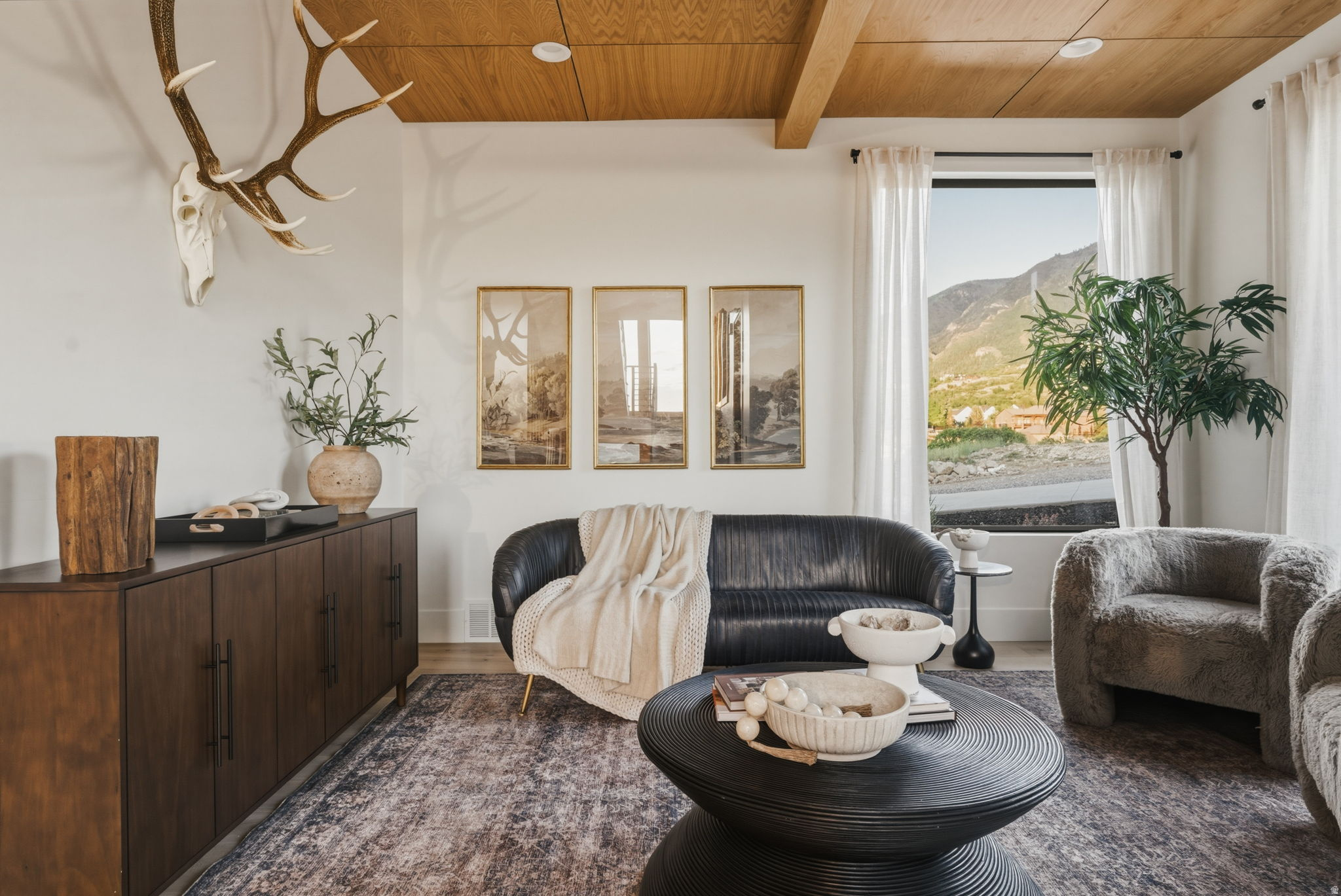 Spacious living area featuring a wood-finish ceiling with exposed beams, a large window with mountain scenery, and light wood-finish flooring