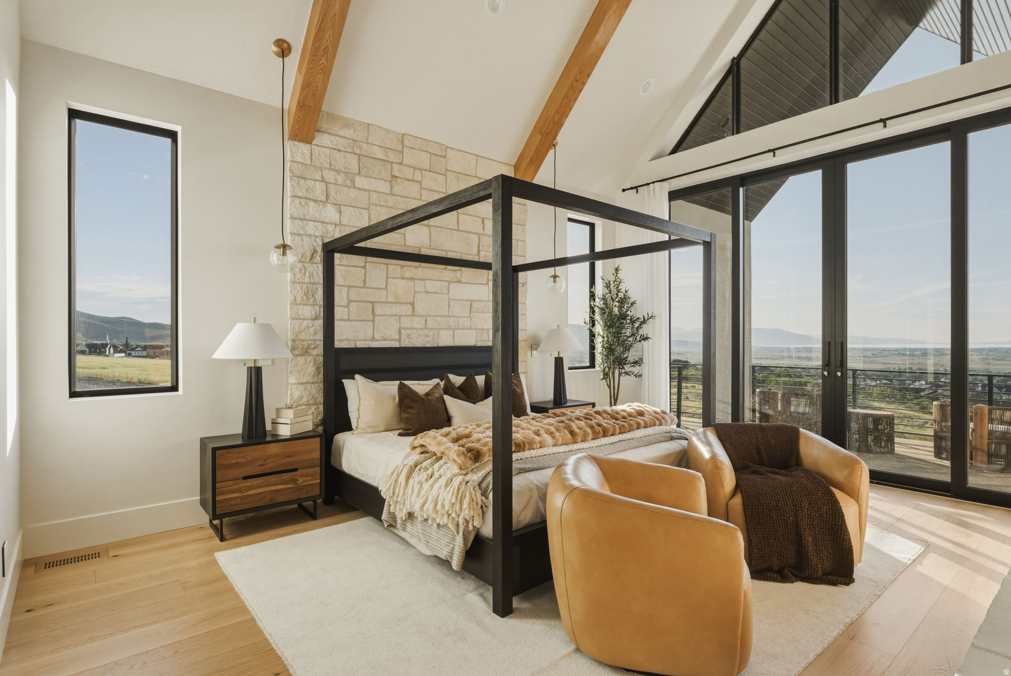 Vaulted ceiling bedroom featuring exposed wood beams, a stone accent wall, and expansive glass doors opening to the exterior