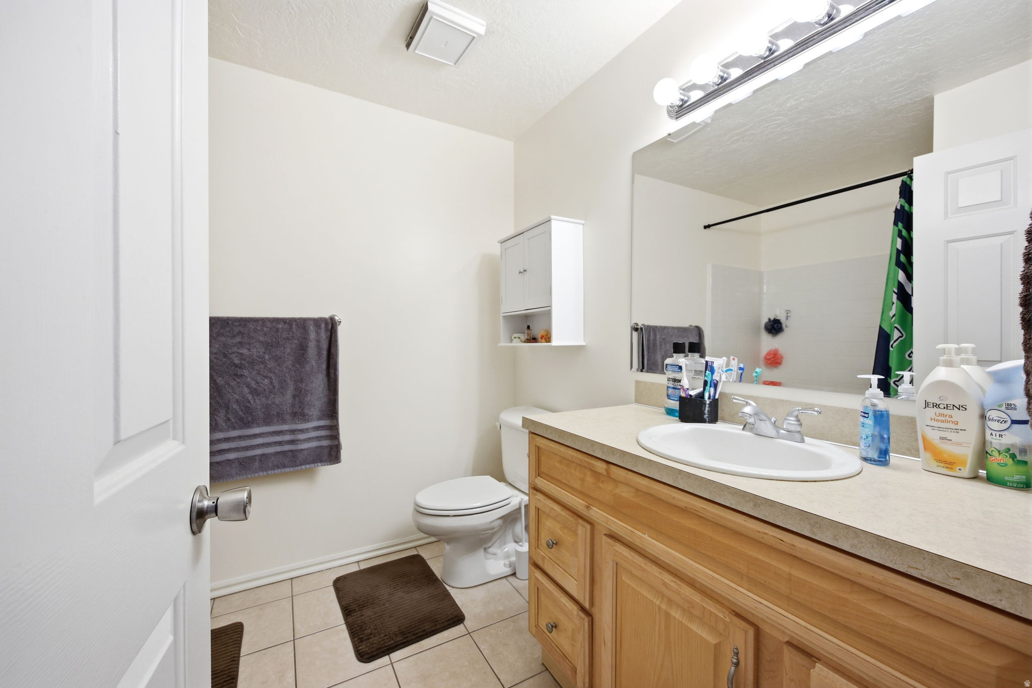 Bathroom featuring a light wood-finish vanity with an integrated sink, a large wall-mounted mirror, and tile flooring