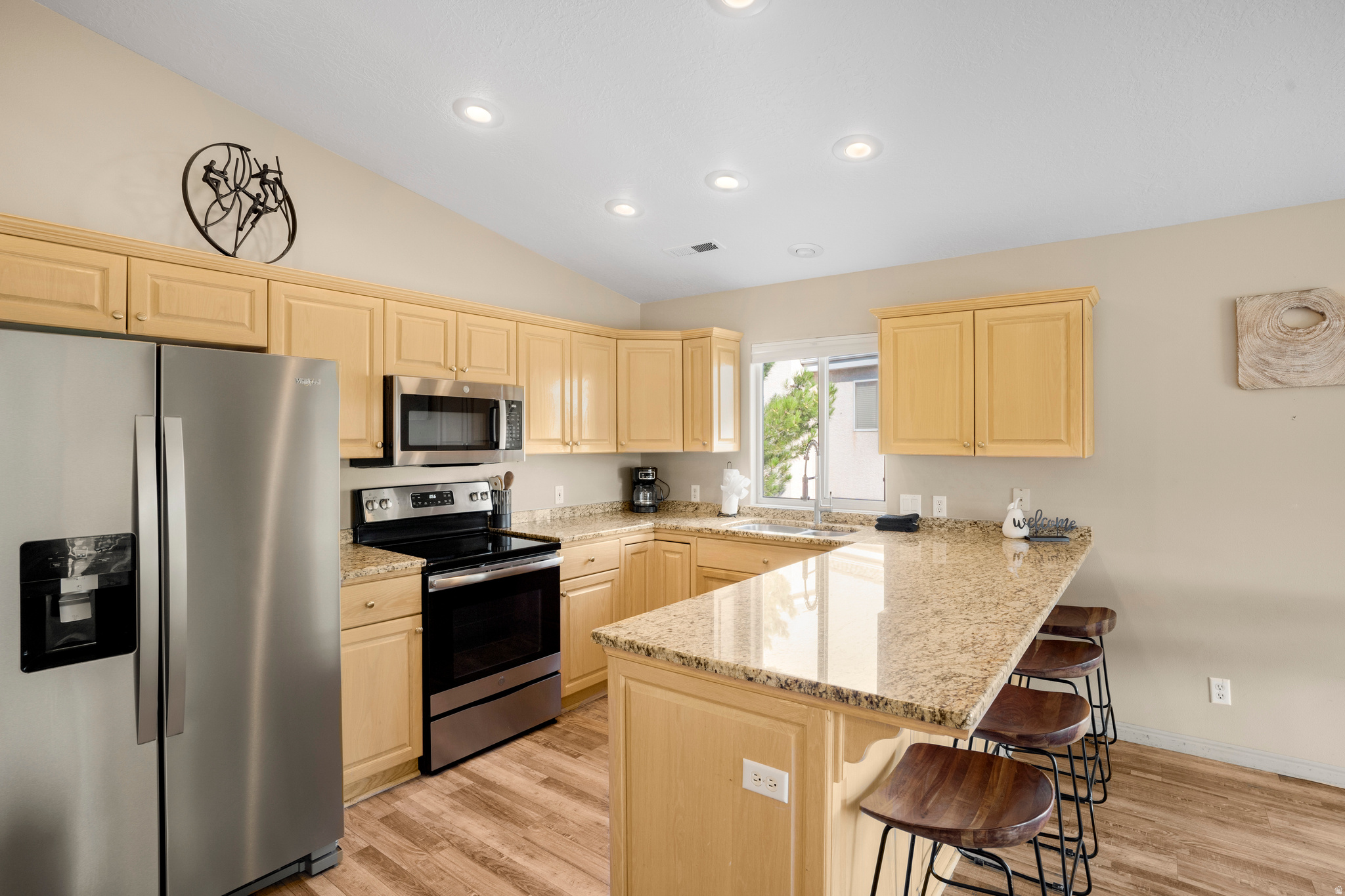 Kitchen featuring light wood cabinetry, stainless steel appliances, a large island with a stone countertop, recessed lighting, and wood-finish flooring