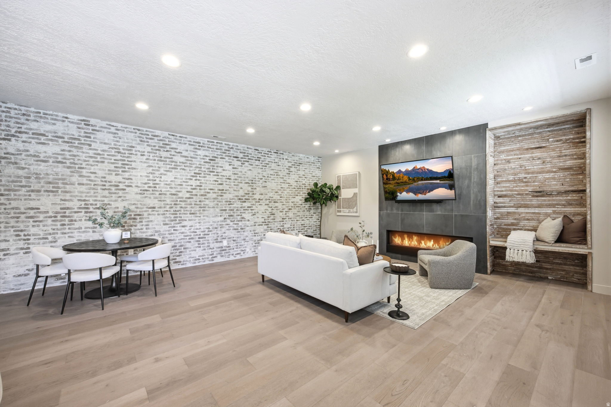 Open-concept living space featuring light wood-finish flooring, recessed lighting, and a whitewashed brick accent wall