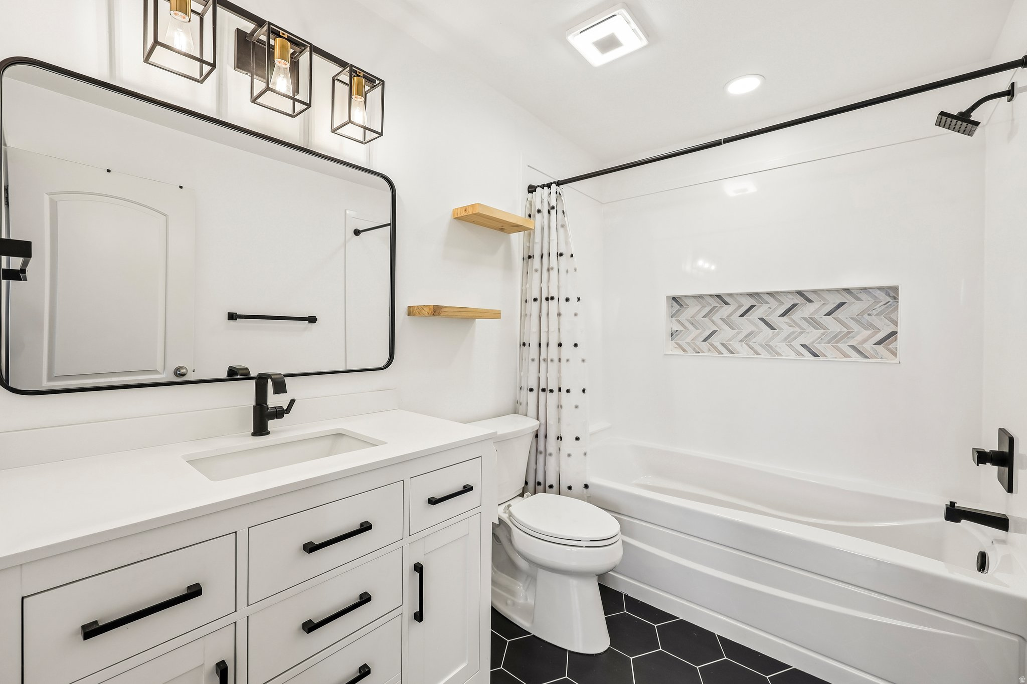 Bathroom featuring a white vanity with integrated sink, black hexagonal floor tiling, and a tub with a tiled niche