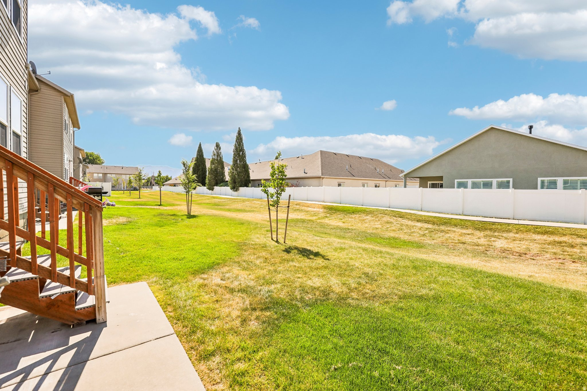 Expansive backyard featuring a green lawn, established trees, and a durable white privacy fence