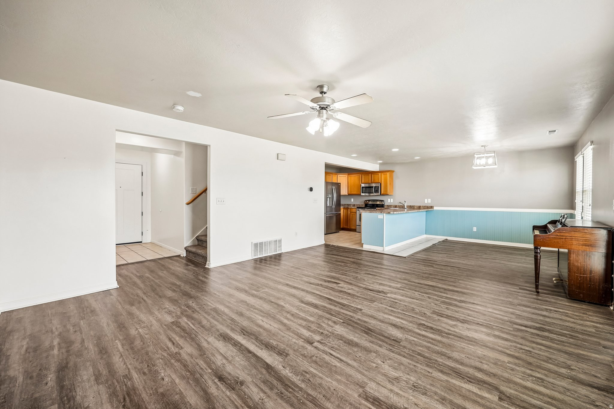 Spacious open-concept living area featuring wood-finish flooring, a ceiling fan with integrated lighting, and neutral wall tones