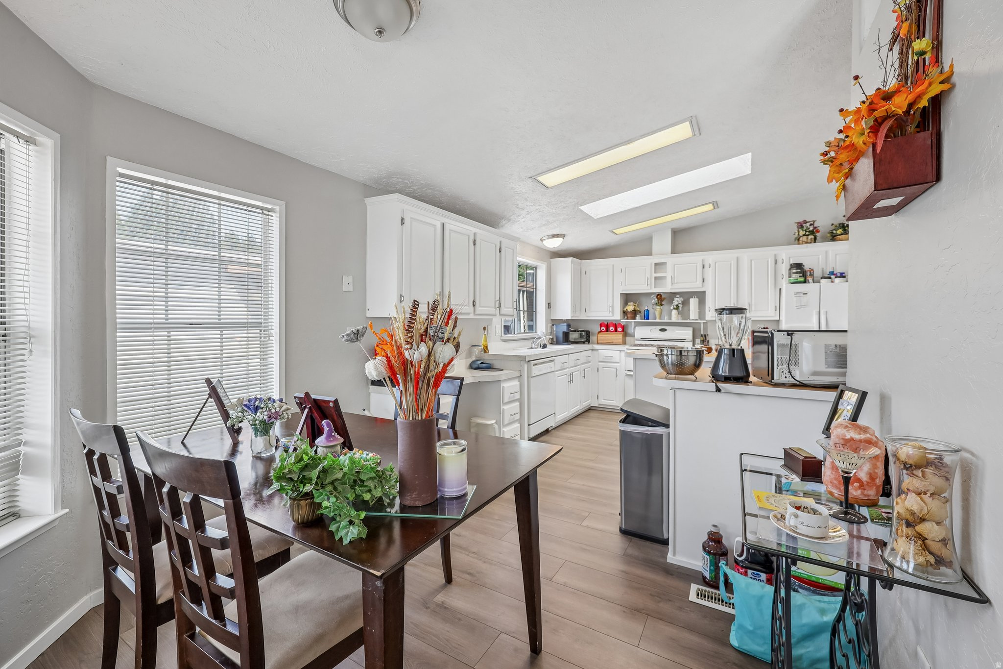Kitchen and dining area featuring wood-finish flooring, white cabinetry, and a vaulted ceiling with integrated lighting