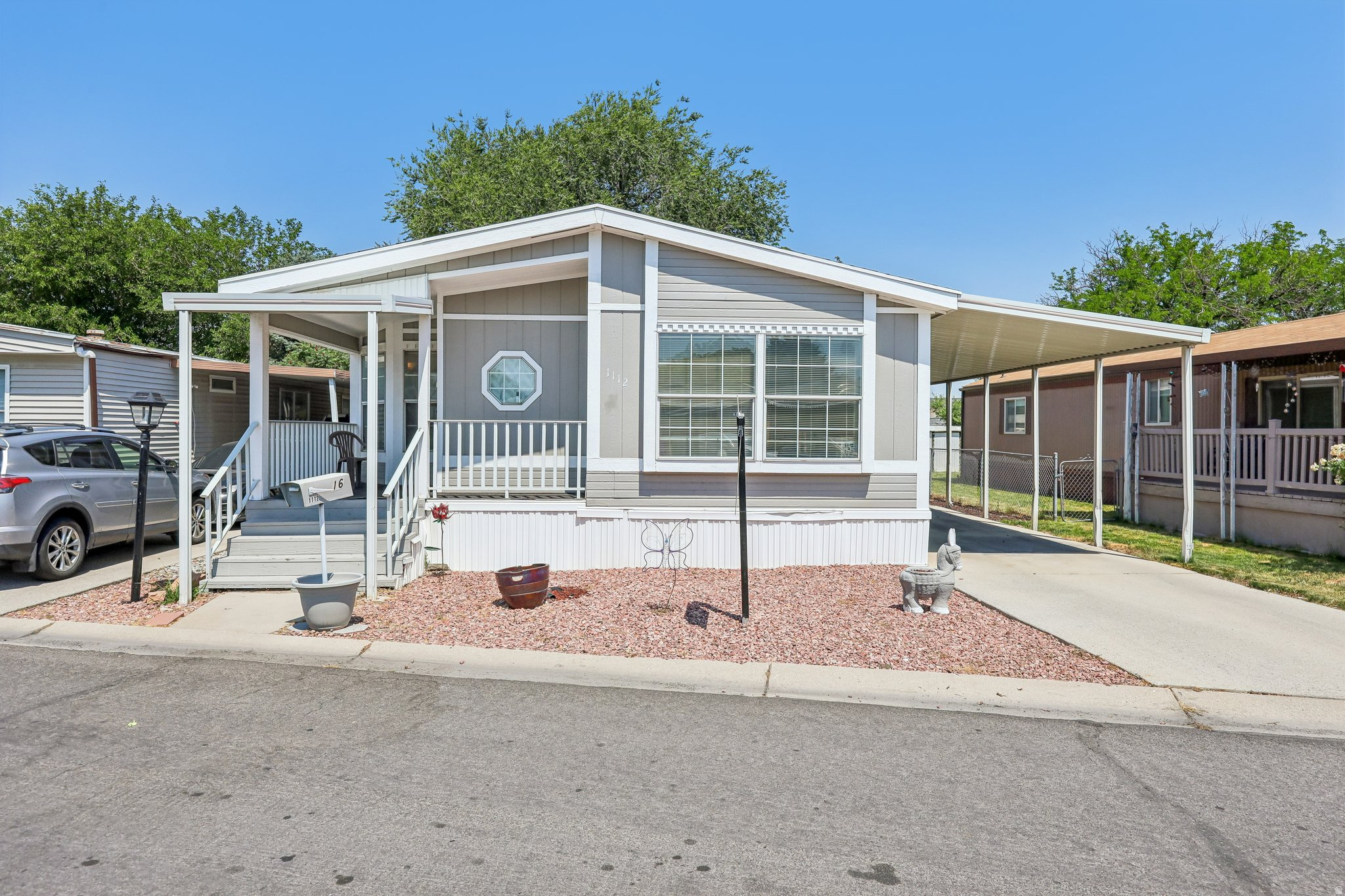 Grey-sided residence featuring a covered front porch, carport, and gravel landscaping