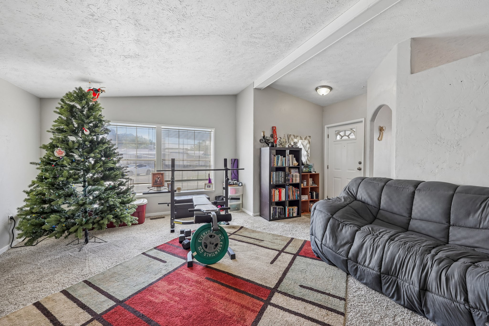 Spacious living area featuring neutral wall tones, textured ceilings, a large window, a partial entryway arch, and a ceiling-mounted light fixture