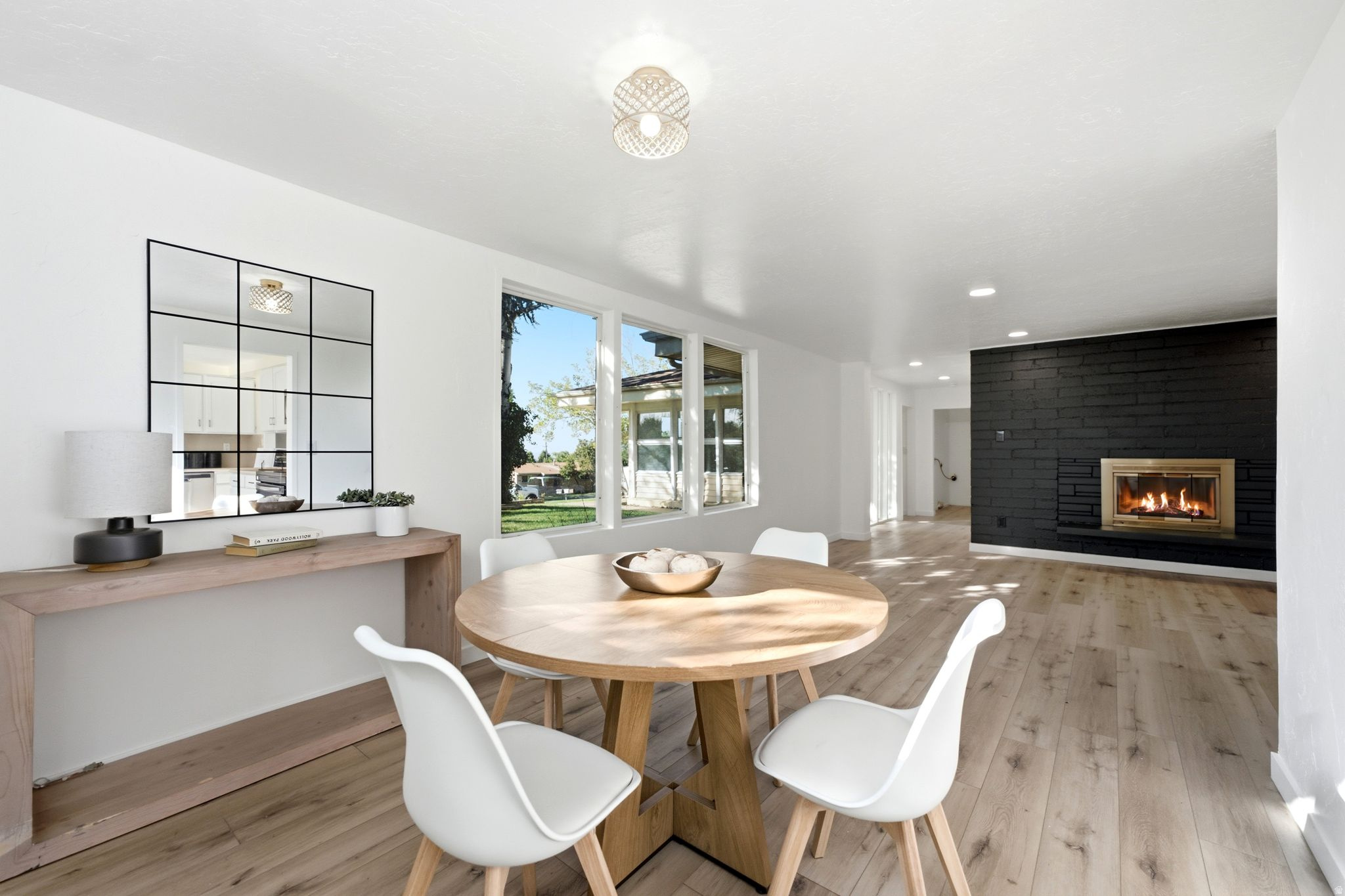 Open-concept living space with light wood-finish flooring, a black brick fireplace, and recessed lighting