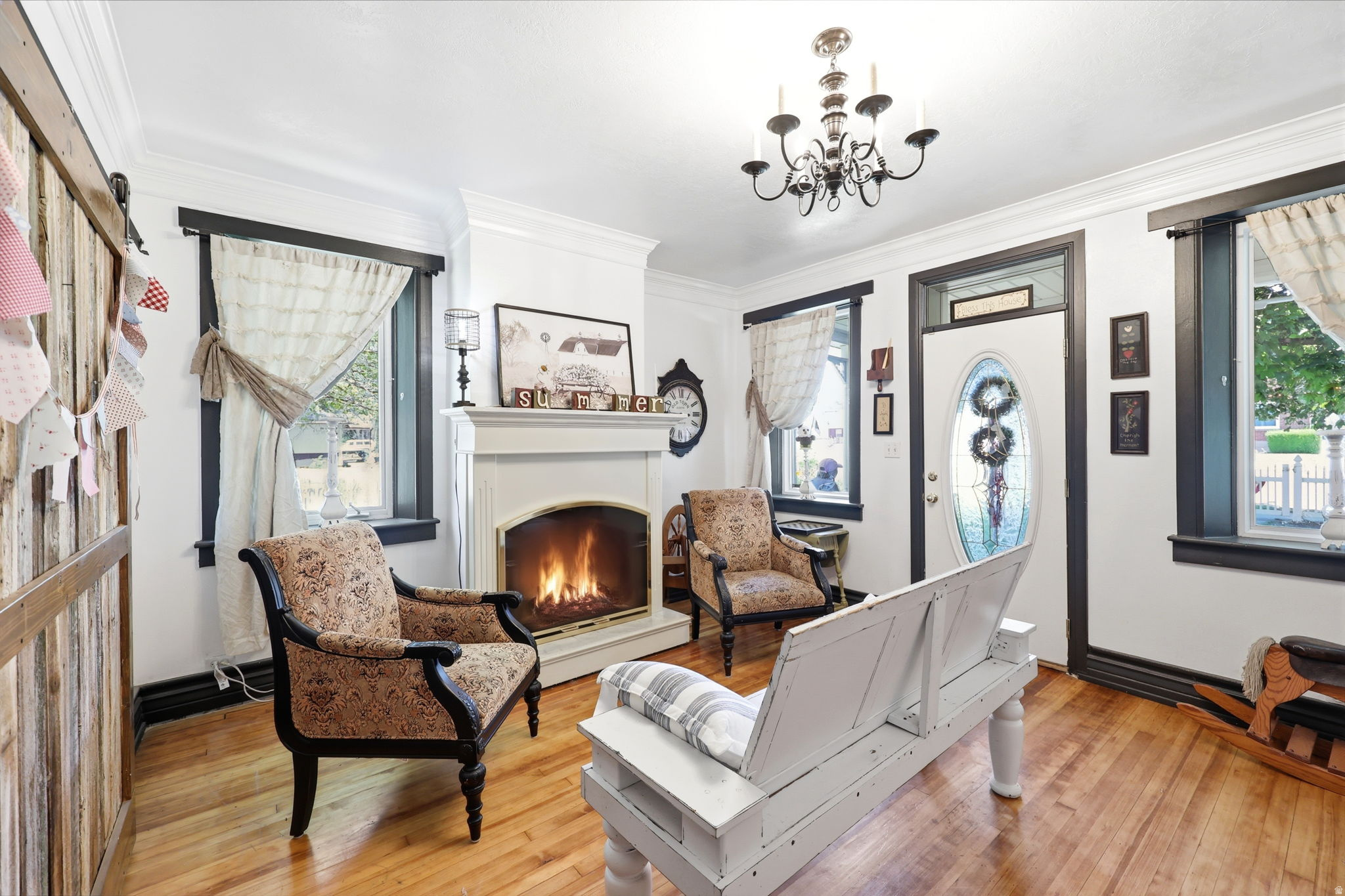 Living area featuring a classic fireplace, crown molding, wood-finish flooring, a decorative front door with an oval glass insert, and dark framed windows