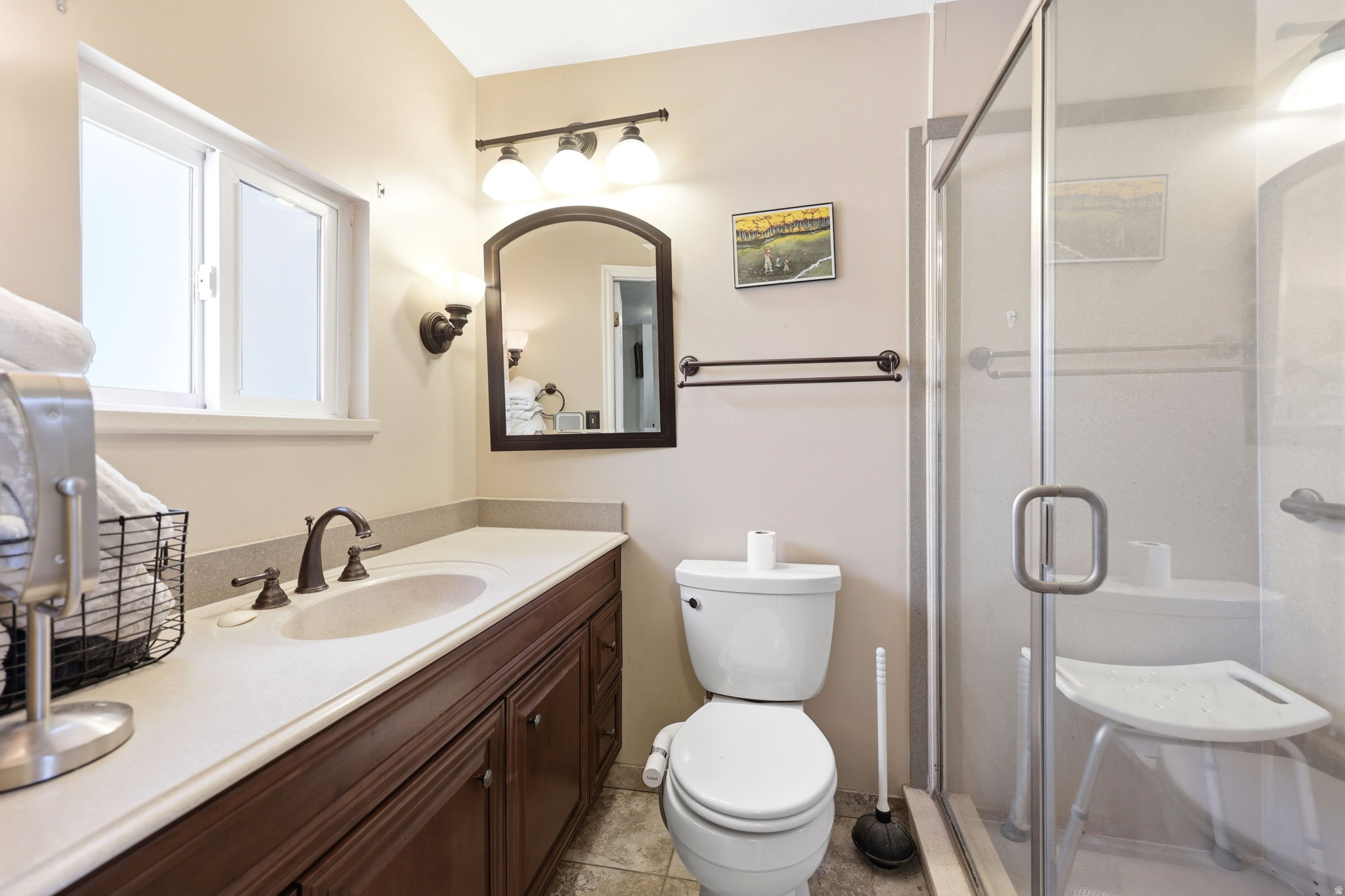 Bathroom featuring a wood-finish vanity with an integrated sink and countertop, a frameless glass shower enclosure, and a window with white trim