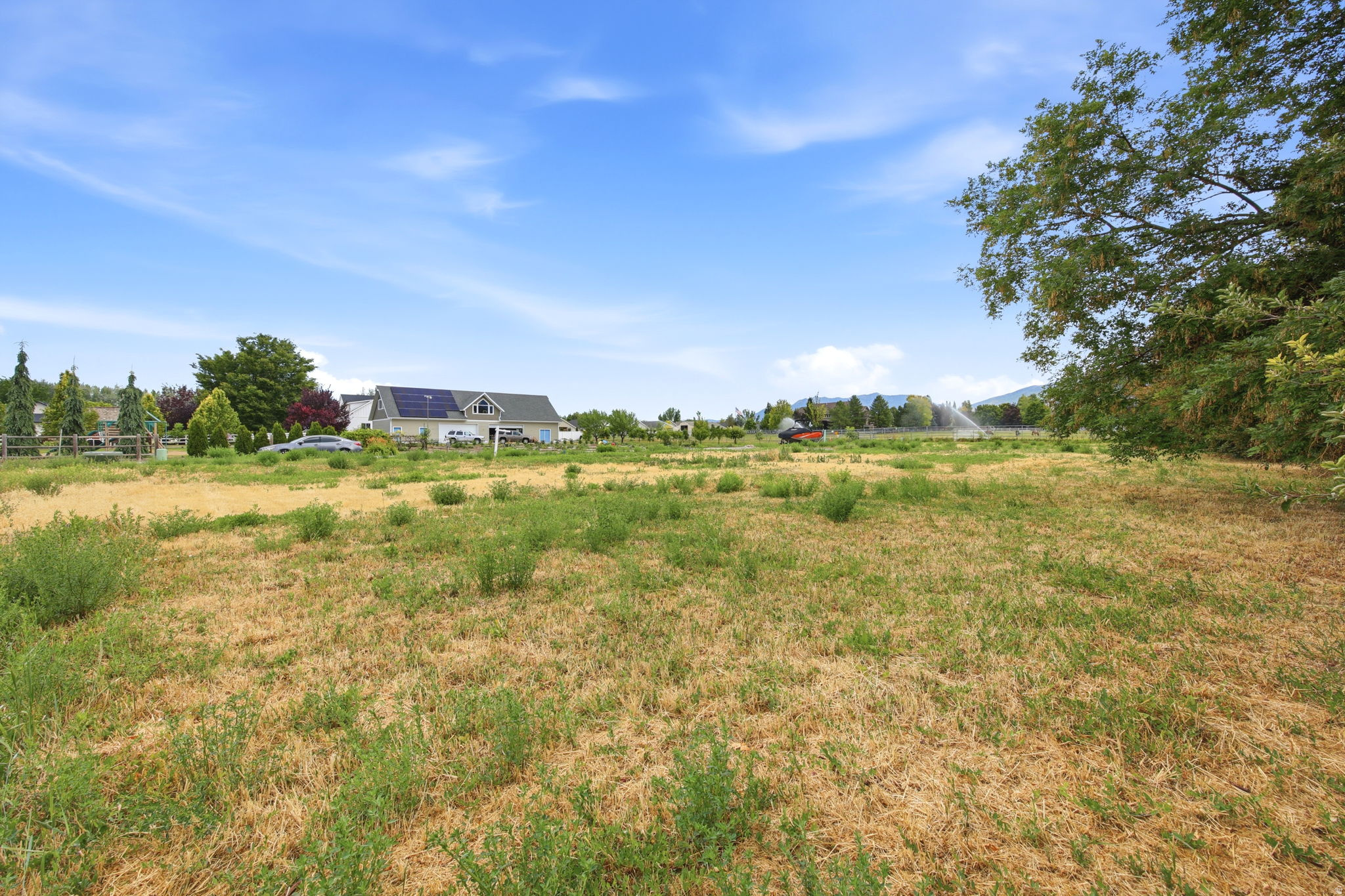 Expansive open lot featuring natural ground cover, established perimeter trees, and distant mountain range