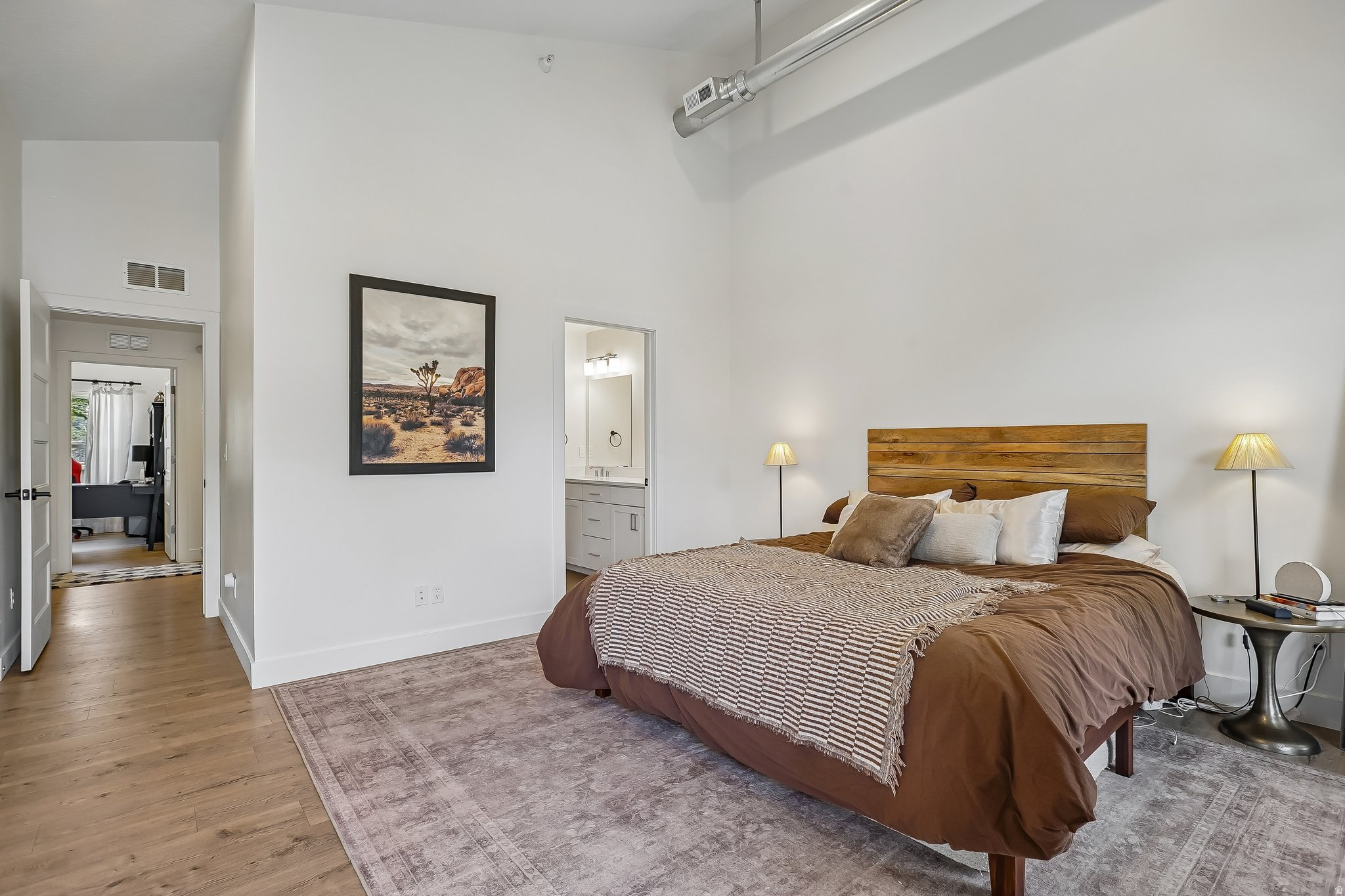 Spacious room featuring high ceilings, exposed ductwork, wood-finish flooring, and a private ensuite bathroom with a vanity