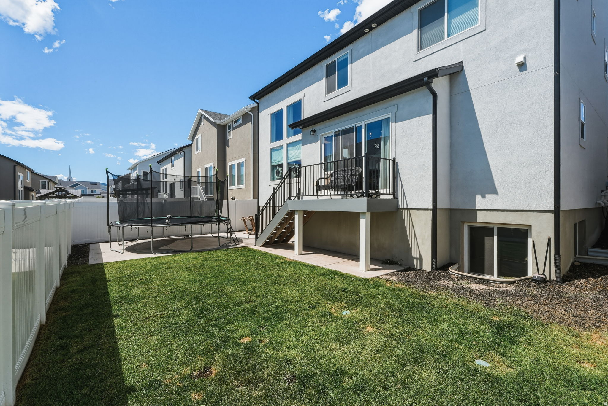 Private backyard featuring a manicured lawn, white vinyl fencing, and a concrete patio