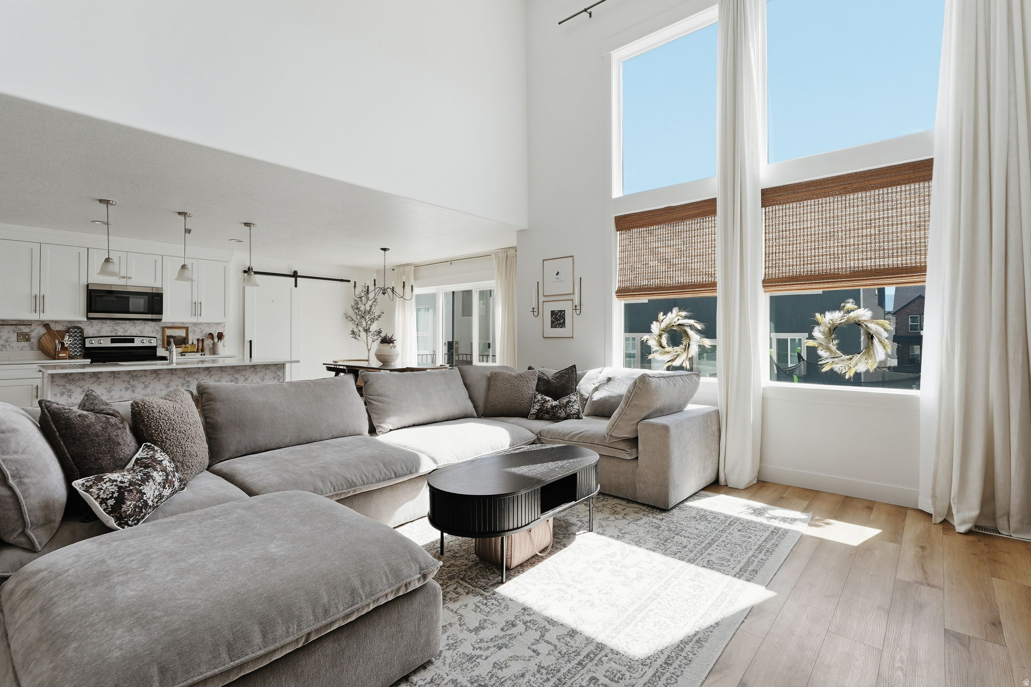 Two-story living area with high ceilings and expansive windows, wood-finish flooring, and an open-concept design that incorporates a kitchen with white cabinetry and a patterned backsplash