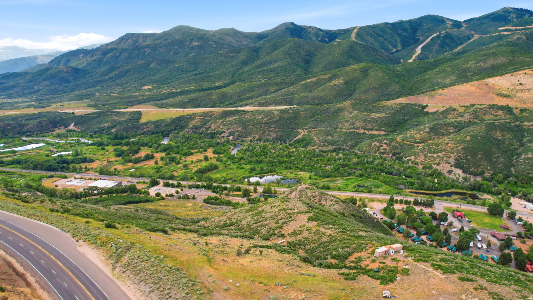 Expansive mountain landscape featuring verdant slopes, natural waterways, and a clear blue sky