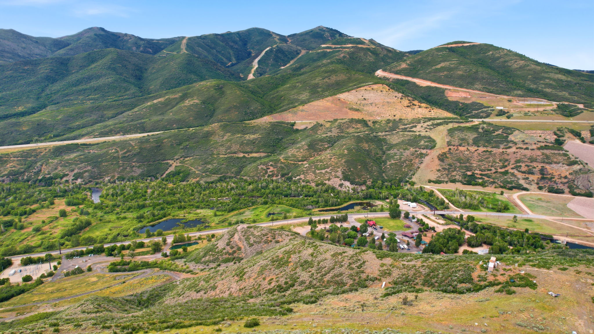 Expansive mountainous terrain featuring a cluster of structures, verdant trees, and two visible bodies of water