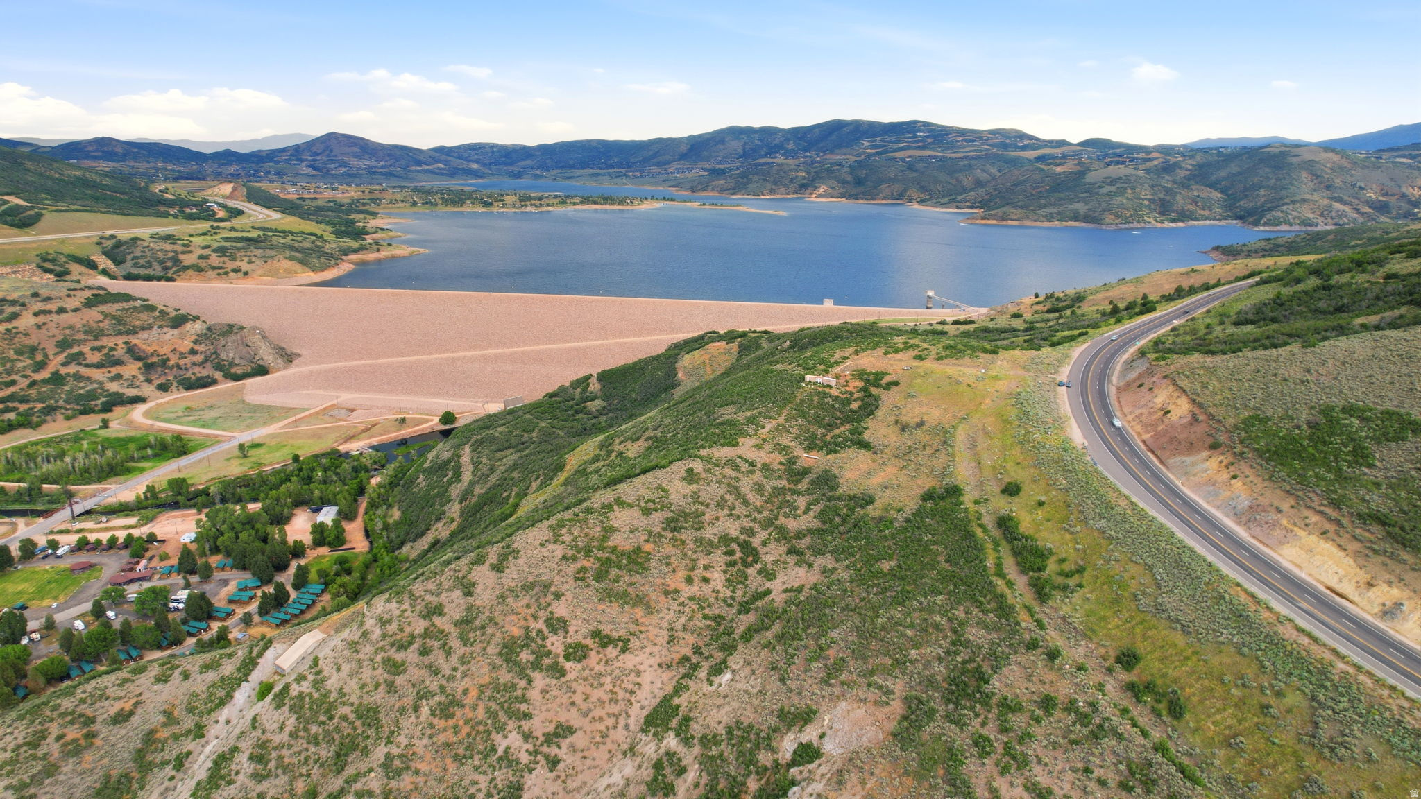 Expansive water feature with a substantial dam structure, surrounded by verdant hillsides