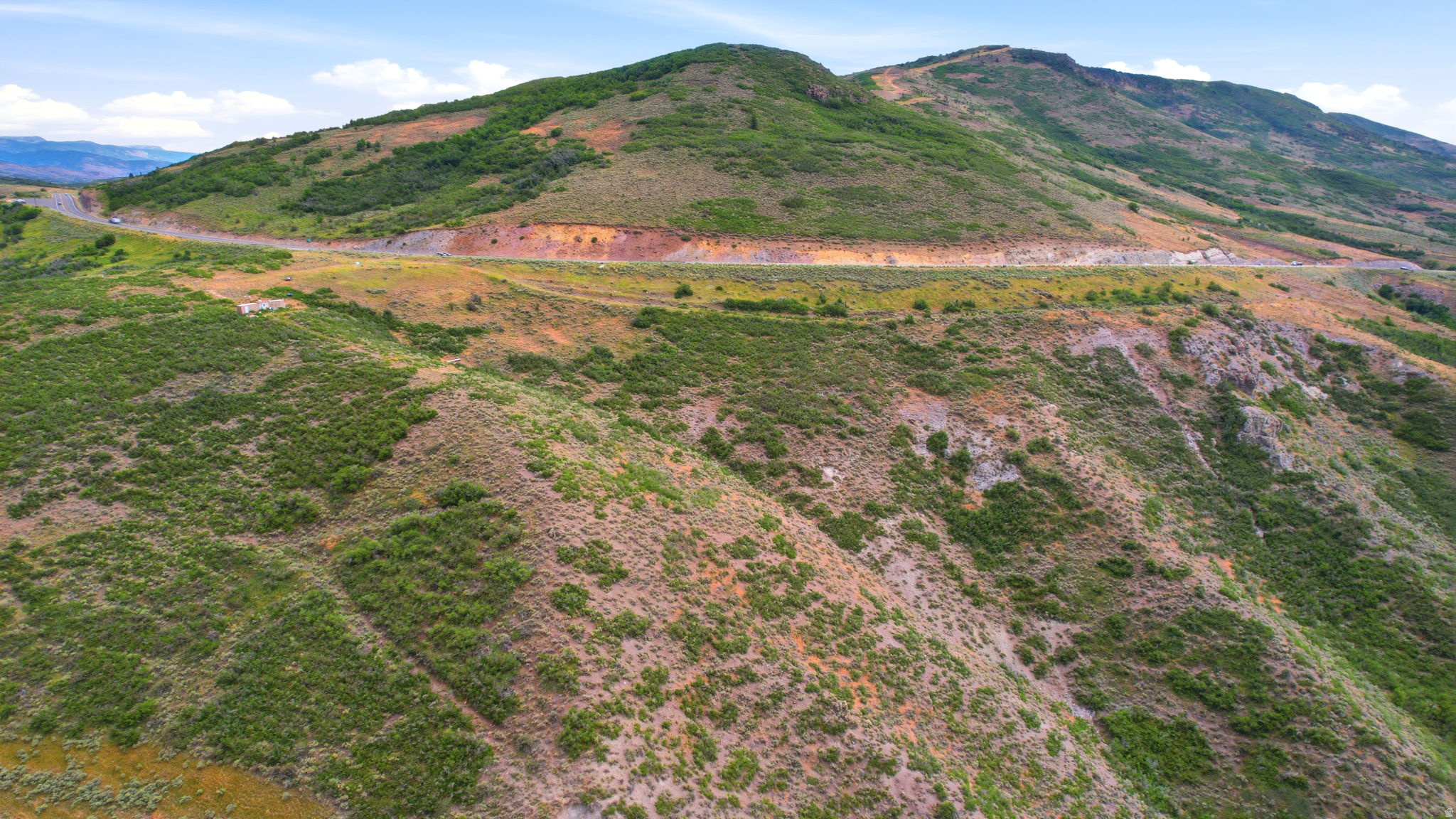 Rolling hills of natural terrain with a winding road across the hillside, featuring expansive natural vegetation and distant mountainous topography