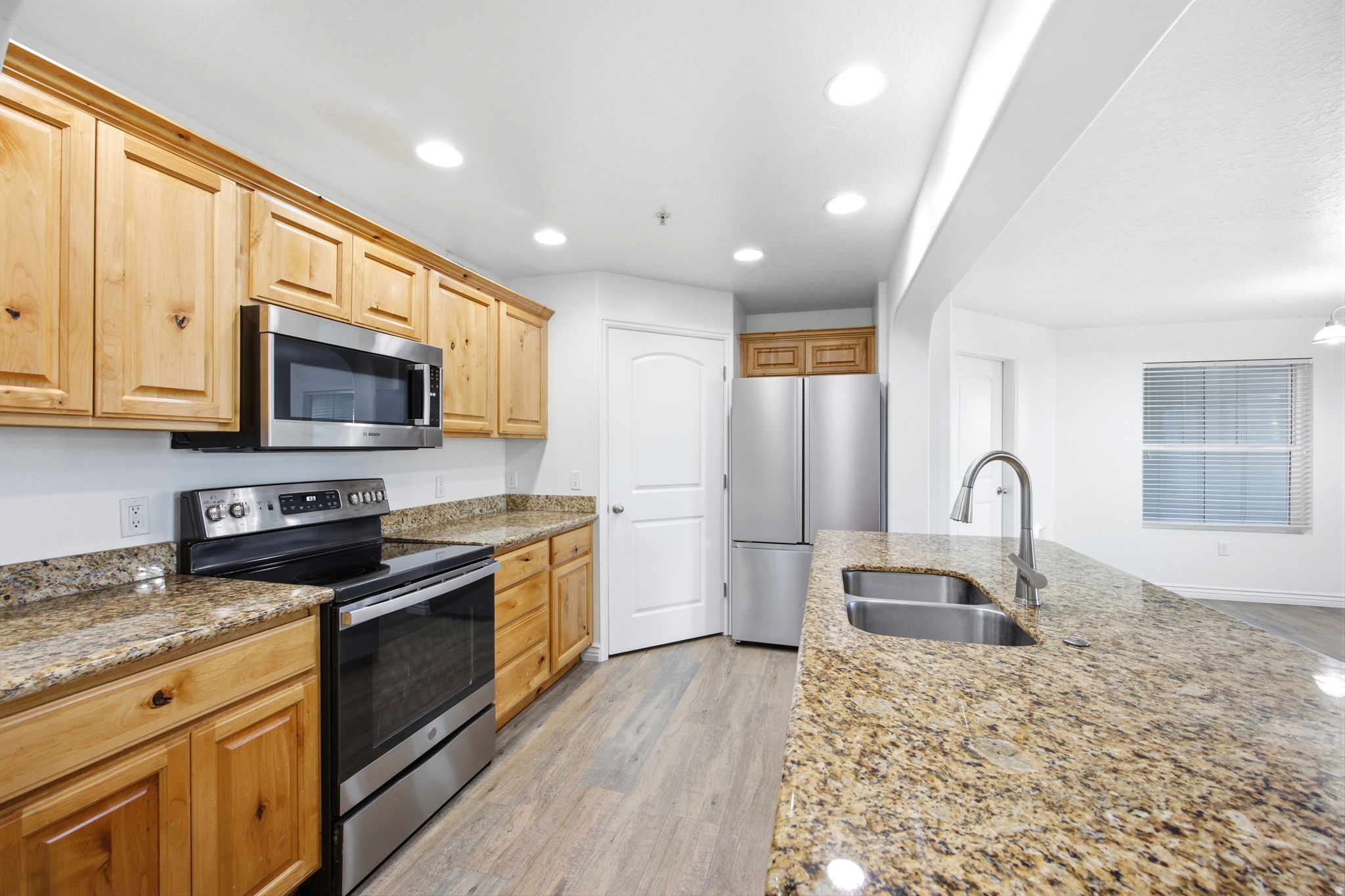 Kitchen featuring wood-finish cabinetry, stainless steel appliances, granite countertops, and wood-finish flooring