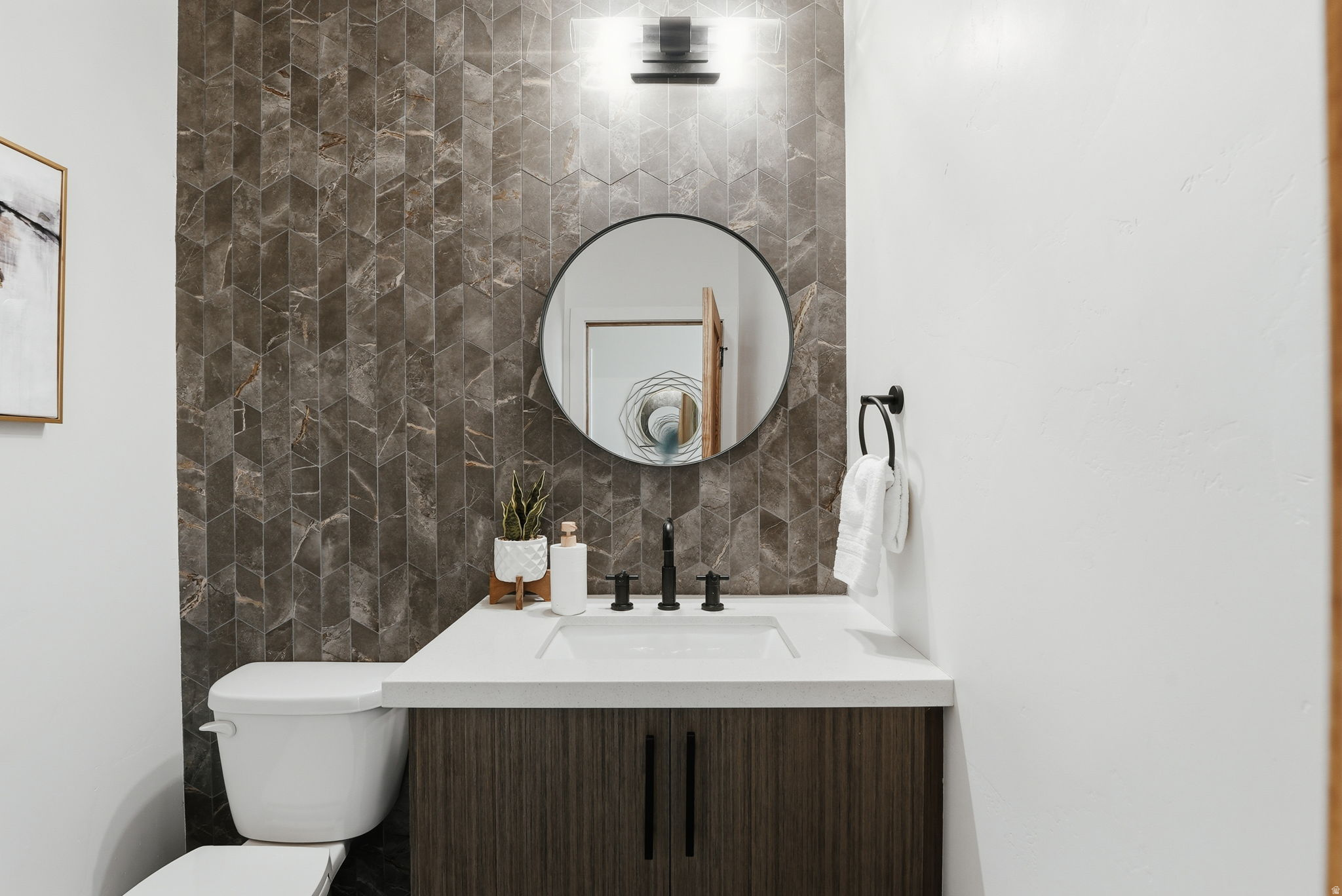 Main floor half bath, vanity with multi-patterned tile accents, white countertop, integrated sink, and wood-finish cabinetry