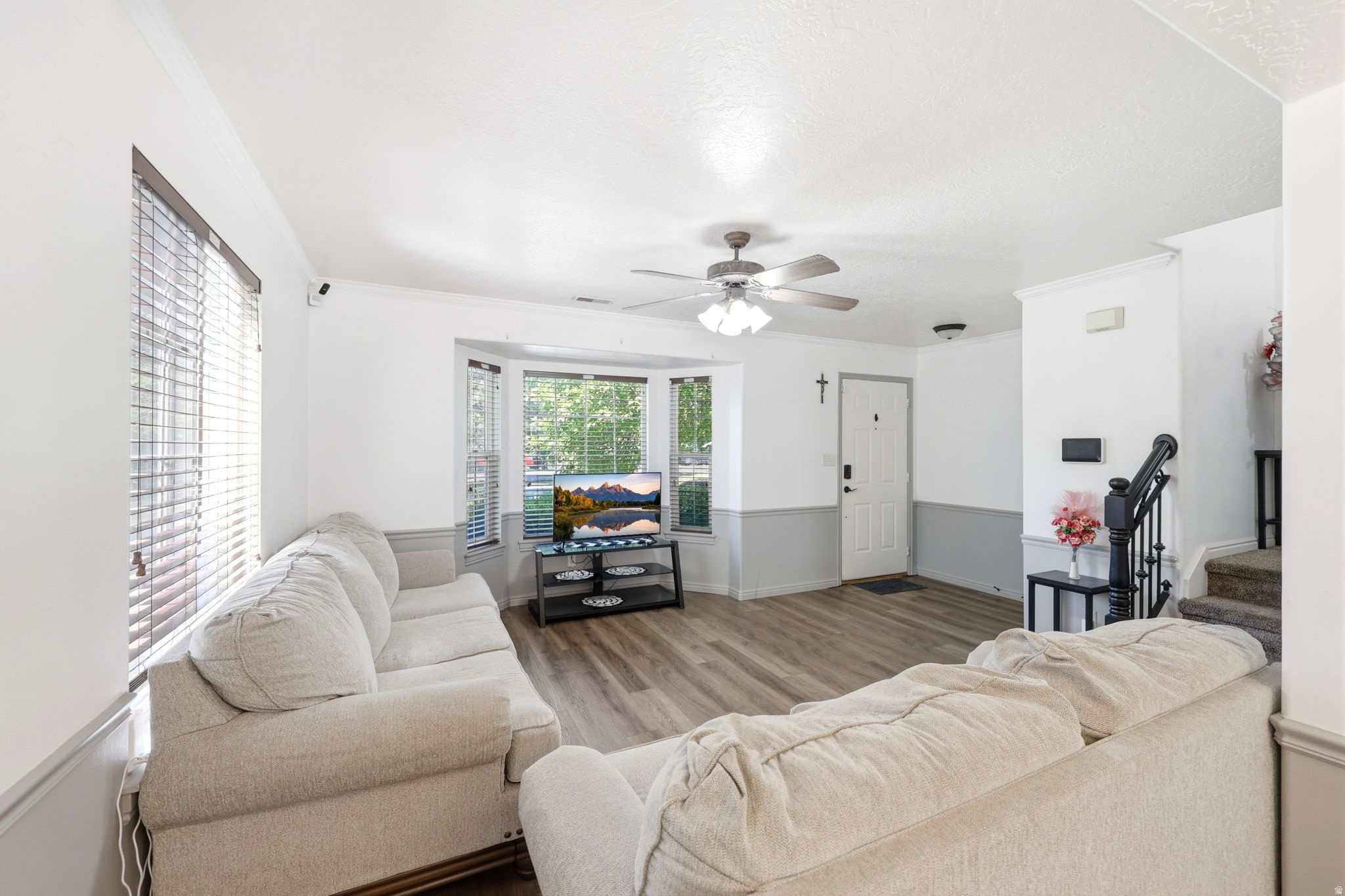 Spacious living area featuring wood-finish flooring, a bay window, and a ceiling fan with integrated lighting