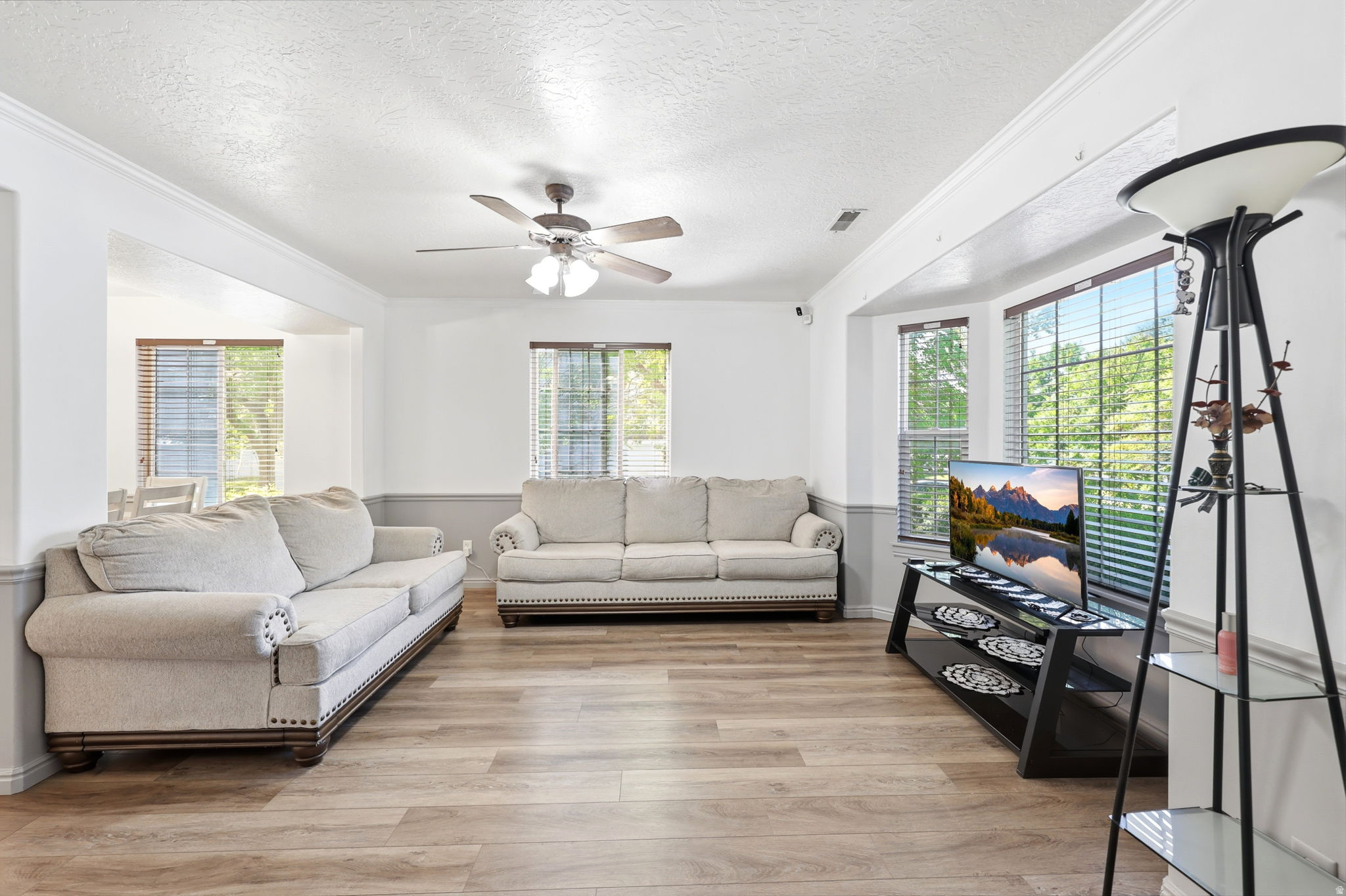 Living area featuring wood-finish flooring, a ceiling fan, crown molding, and a bay window