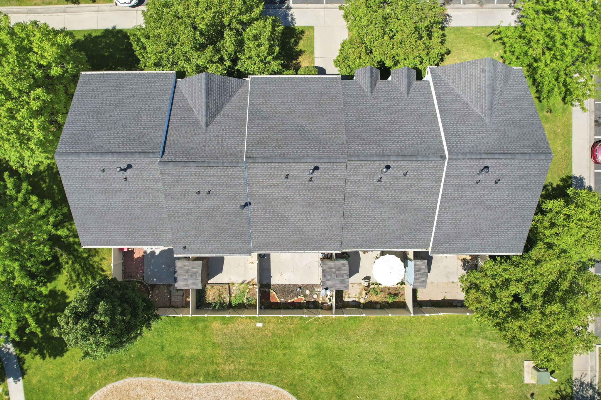 Townhome row with dark gray shingle roofing, individual rear patios, and a shared green space