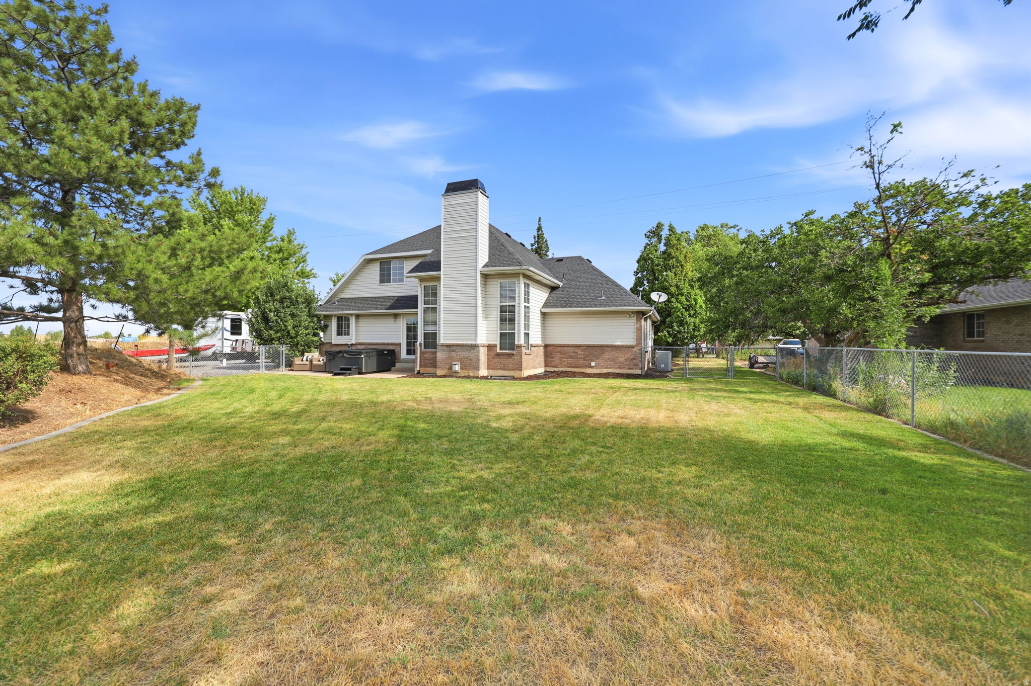 Spacious backyard with a two-story residence featuring a white siding exterior, brick accents, a prominent chimney, and a dark shingled roof