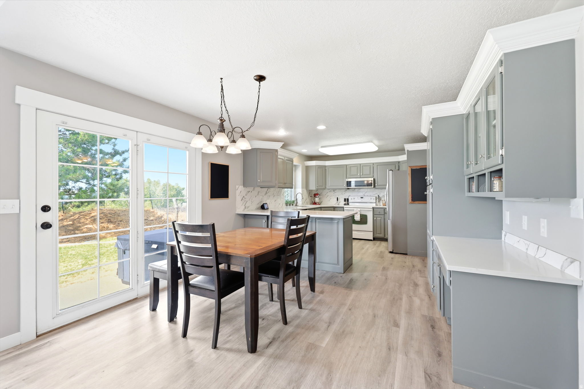 Open-concept kitchen and dining area featuring light wood-finish flooring, a kitchen island with seating, grey cabinetry, white countertops, and a white tile backsplash