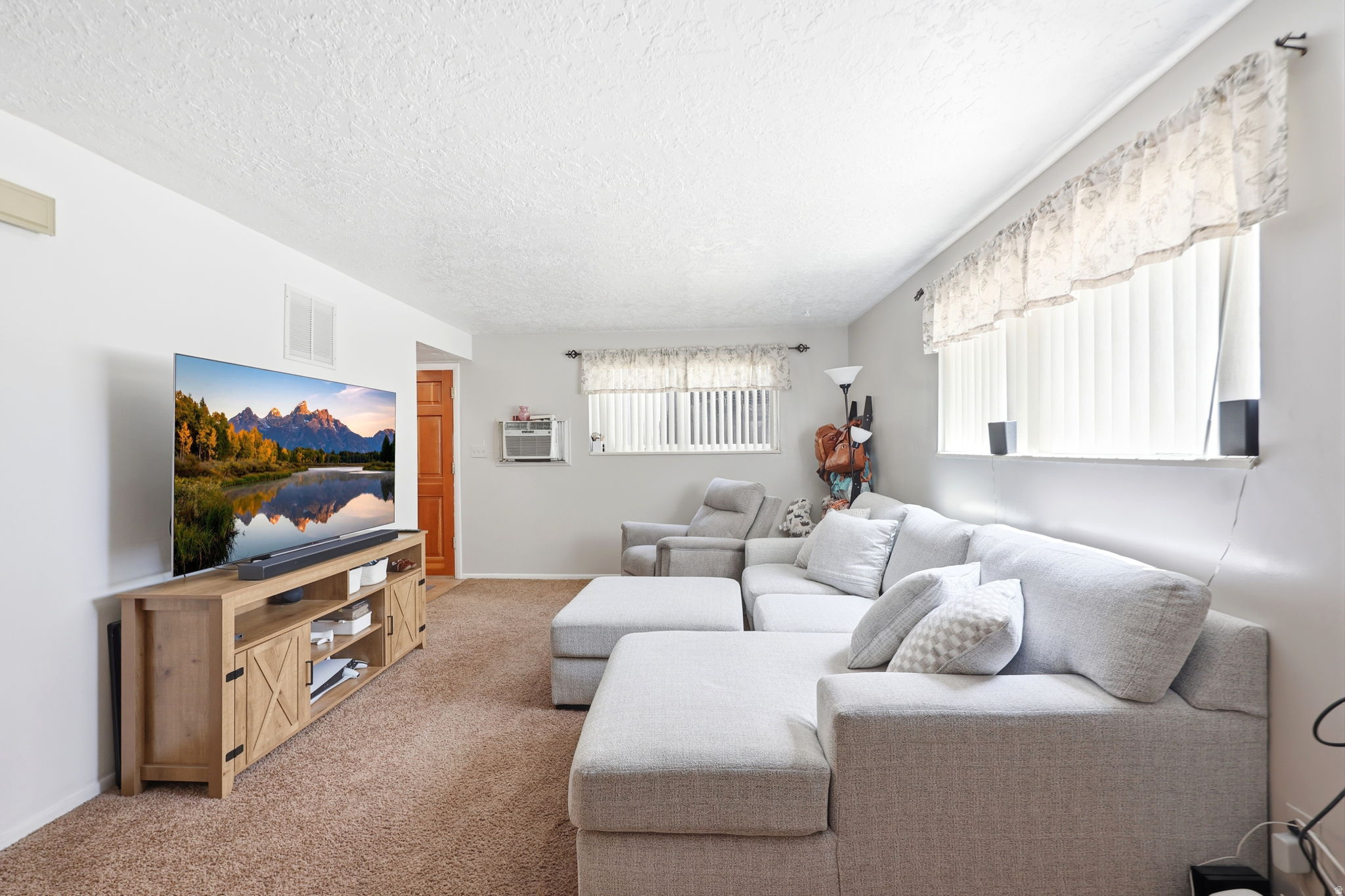 Carpeted living area featuring white walls, a textured ceiling, and natural light from multiple windows