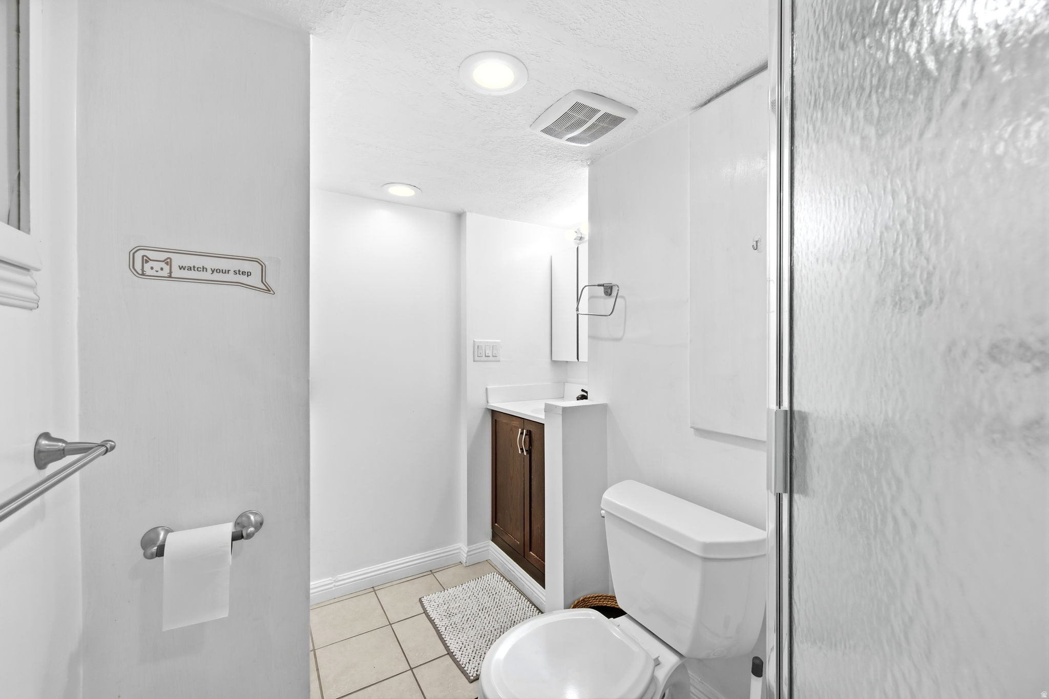 Compact bathroom featuring a glass shower enclosure, recessed lighting, and a dark wood-finish vanity with a white countertop