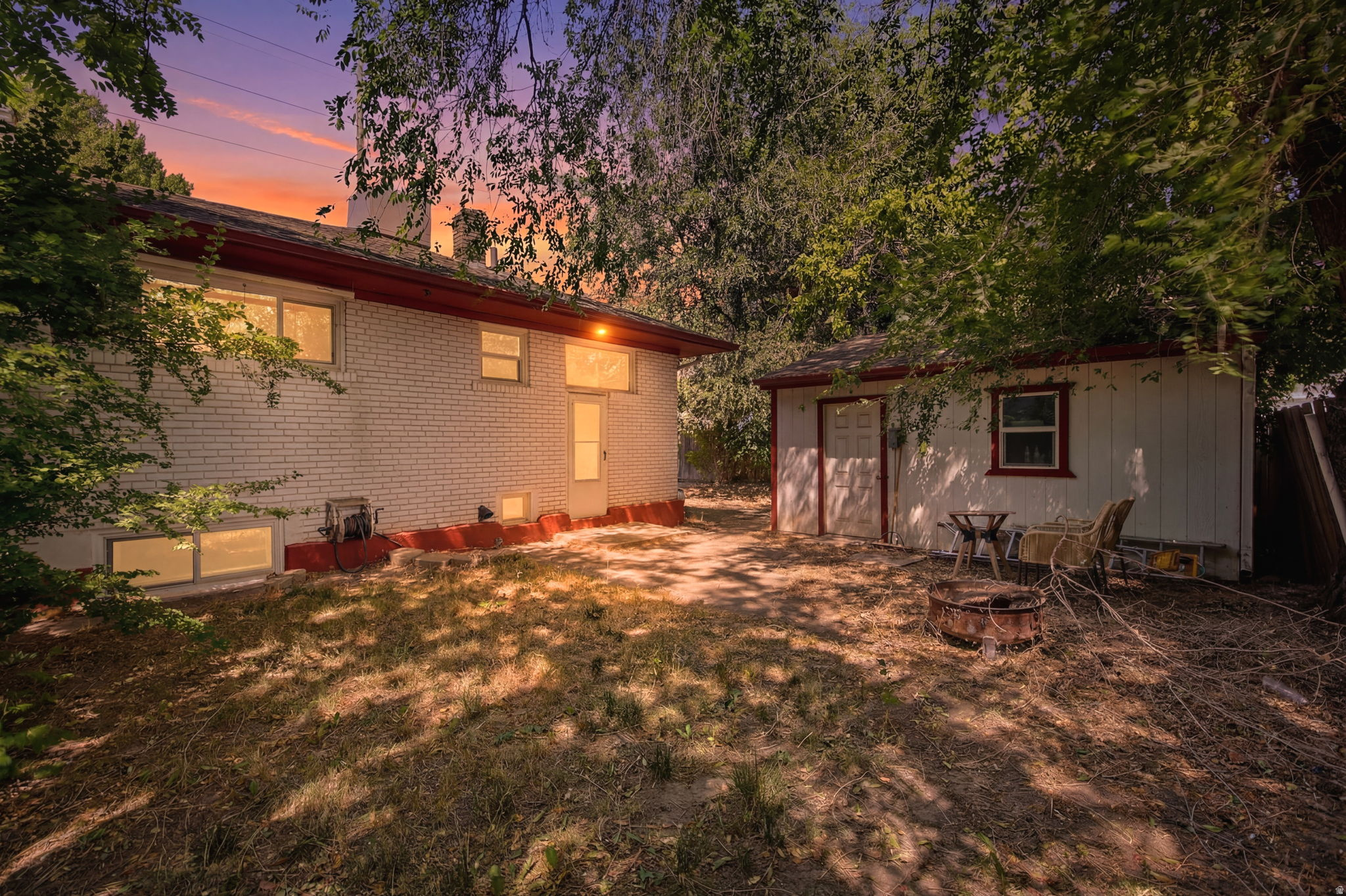 Spacious backyard featuring a white brick exterior, an exterior door, multiple windows, and a separate storage shed with a white and red exterior