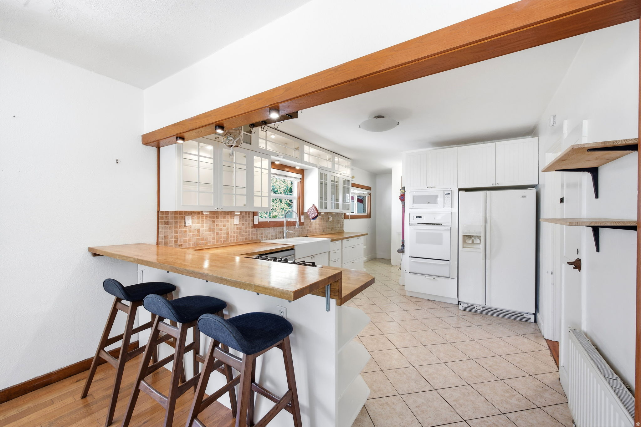 Kitchen featuring a breakfast bar with wood-finish countertop, white cabinetry, integrated built-in appliances, tiled flooring, and a tiled backsplash