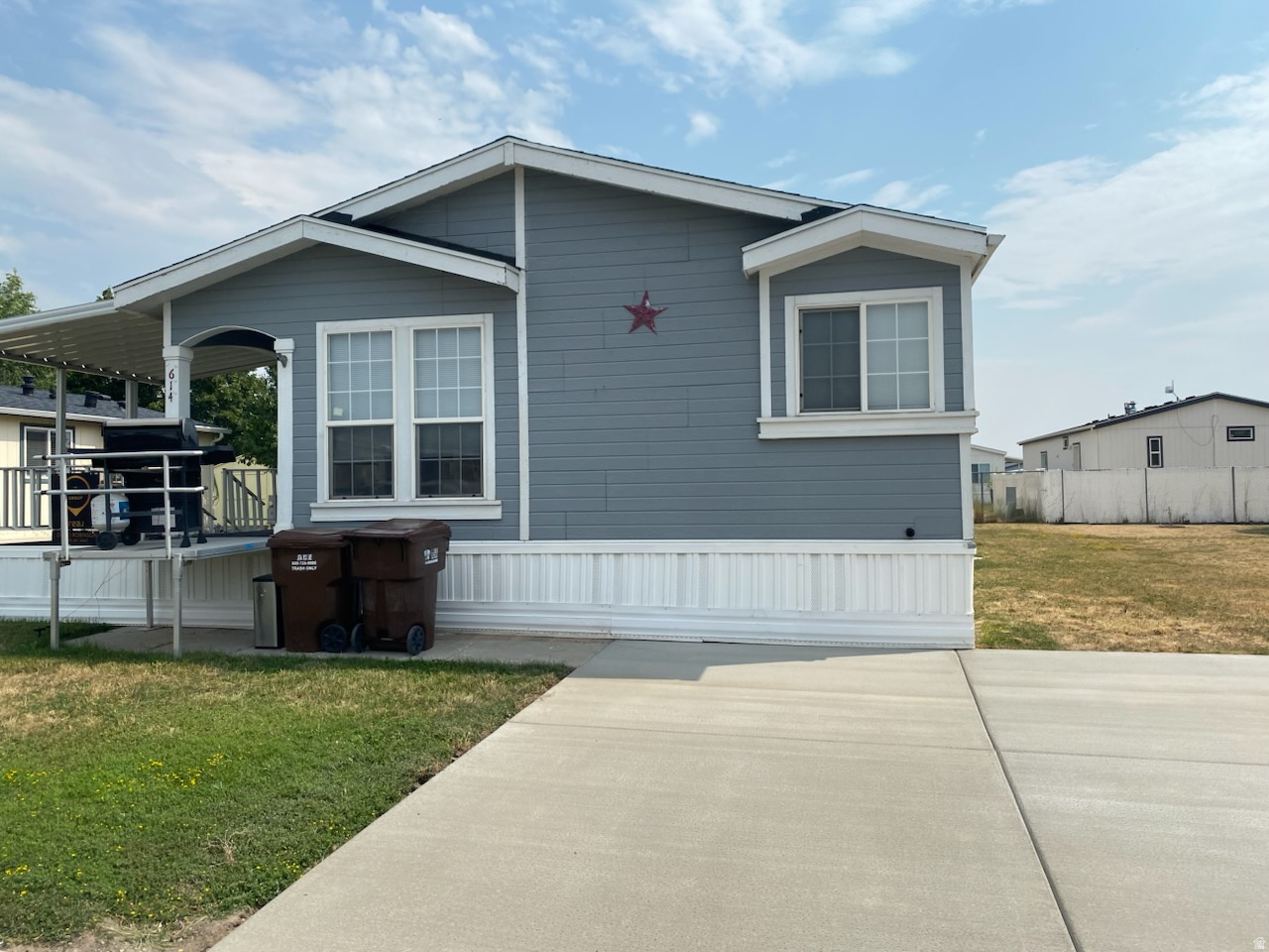 Manufactured home featuring blue siding with white trim, a covered porch, and a freshly repaired concrete driveway