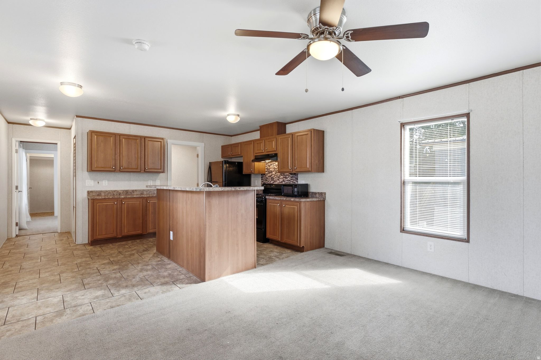 Open-concept living area featuring a kitchen island, wood-finish cabinetry, black appliances, and a tiled backsplash